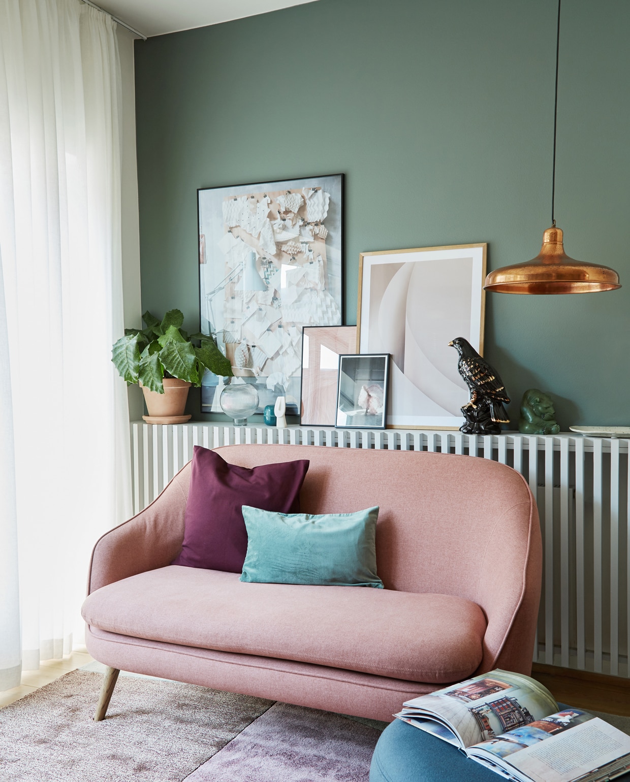 Vloerkleed van Please wait to be seated, gordijnstof Jab. Bank van Sofacompany. Radiatorombouw zelfgemaakt voor items die ze nergens kwijt konden in het huis zonder vensterbanken. Grote poster werk van Anitta uit het boek Arts and Crafts Homes, roze print en lichte poster By Garmi, klein plaatje Dos Family. Kussens H&amp;M Home. Lamp vlooienmarktvondst. Poef Warm Nordic. Muurverf Vineyard nr. 61 van Flügger.