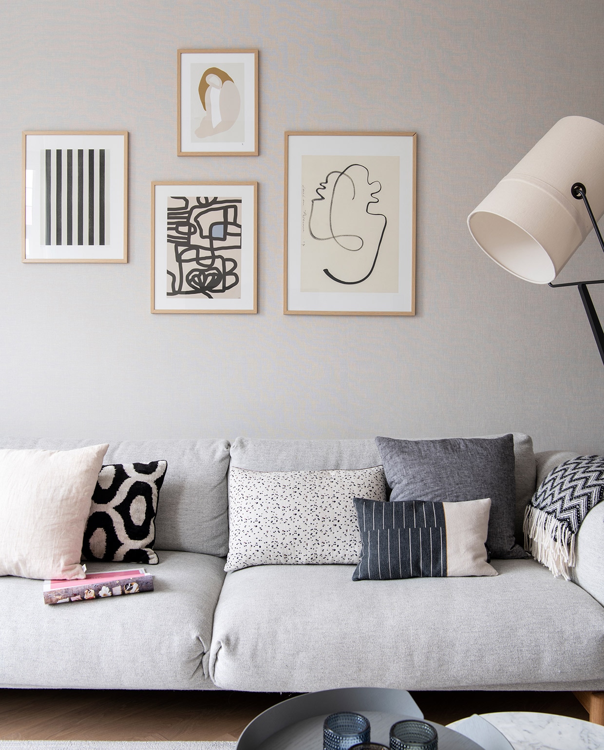 Bank Muuto. Kunst aan de muur via The Poster Club in eiken lijsten van Bolia. Kussens v.l.n.r.: wit By Mölle, wit met zwart patroon Koya Living, wit met zwarte stippen Pom, deels zwart deels wit Mae Engelgeer, antraciet By Mölle. Plaid Elvang Denmark. Waxinelichthouders Iittala. Vloerlamp Diesel.