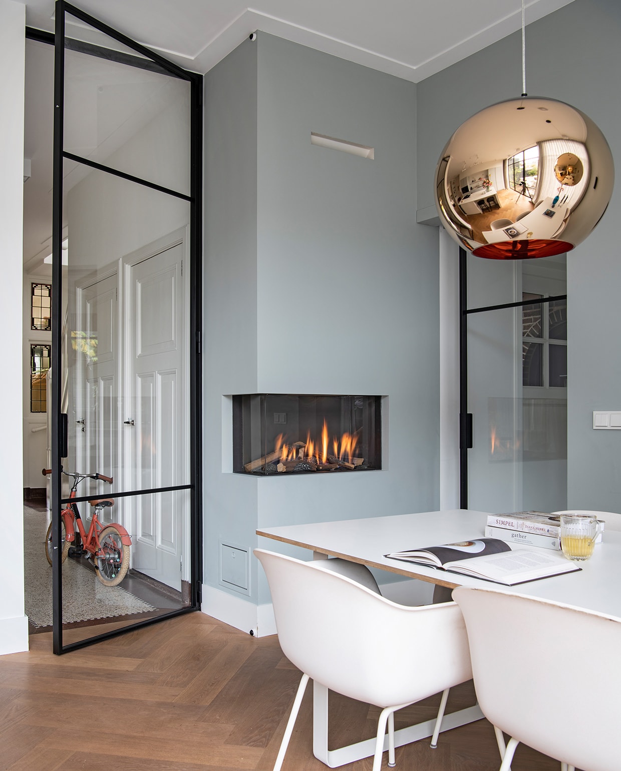 Muurverf Light Blue 22 van Farrow &amp; Ball. Vloer eiken. Tafel en stoelen Muuto. Hanglamp Tom Dixon. Glas HKliving. Elektrische open haard Element4. Fiets Veloretti. Glazen deuren gemaakt in Polen.