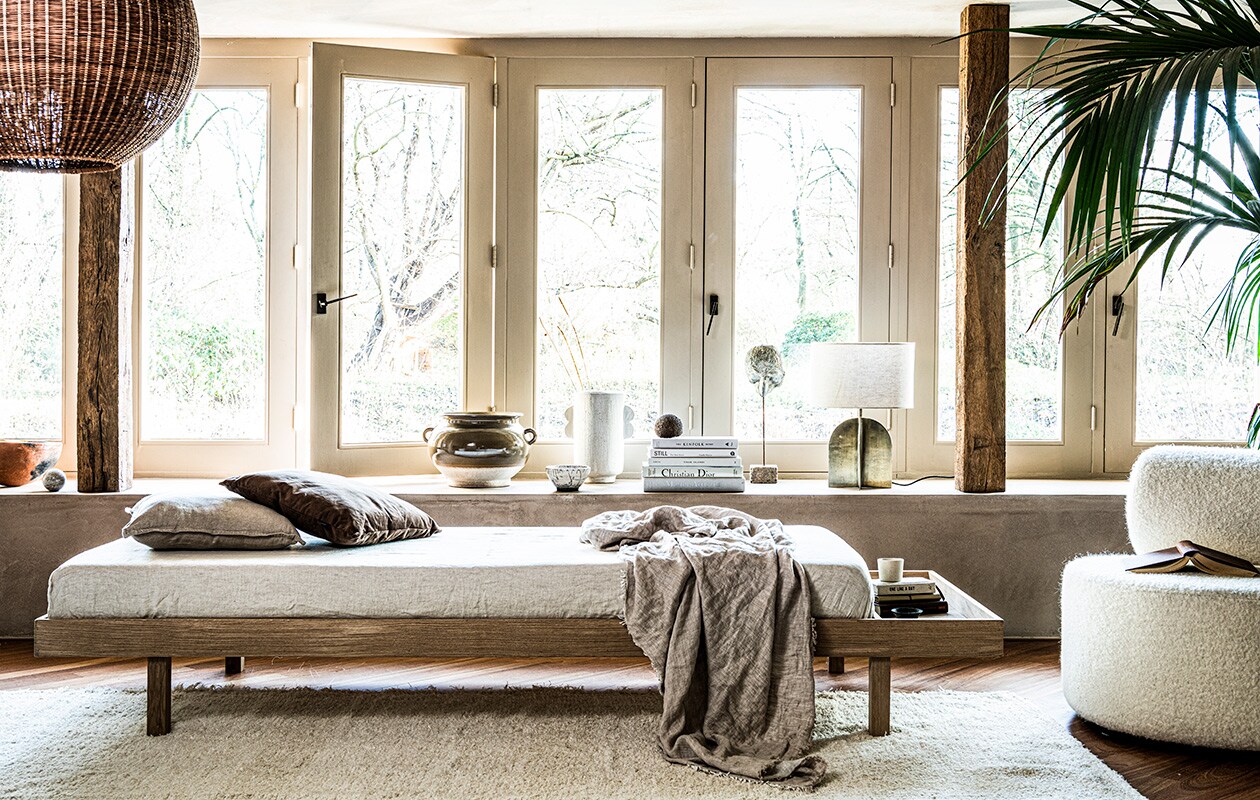 Hanglamp Bamboo van hkliving 55,5 cm hoog, Ø 60 cm, bruin ribkussen van Essanza 45×45 cm (vtwonen.nl). Vloerkleed 200×300 cm, linnen deken 140×190 cm, lamp met goudkleurige metalen voet, verwassen linnen onderlaken, linnen kussenhoes 45×45 cm, bruine pot met oortjes (zarahome.com). Fauteuil Sinclair teddy (festamsterdam.com). Beige aardewerken vaas met darius-oortjes van Urban Nature Culture (sissy-boy.com). Overig privébezit.
