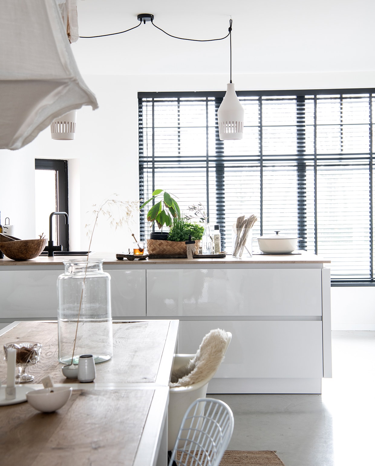 Keuken Superkeukens, raambekleding 123Jaloezie, hanglampen vtwonen. Witte pan Ikea, kraan Selsiuz via Superkeukens, houten spatels en kommen Van Hees Design, plant en plantenpot Budgetplant. Tafels uit een faillissement van een lunchroom, hanglampen vtwonen, draadstoel Jos Met Stijl, Eames-stoel Loods 5, vacht Vacht van Vilt. Kaarsen- standaard The Loving Wonen, schaaltjes en vaasjes Boet-Stijl, glazen vaas kringloop Allerhande Panningen.