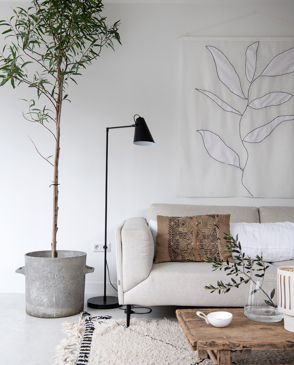 Bank Feelings Wonen, bruine kussens uit Marrakech, overige kussens en kunstwerk Huize Jolie. Plant Budgetplant. Vloerlamp vtwonen. Kleed Marktplaats, koffietafel Cooperz Wonen, vaas Hoy Concept Shop. Bloempot Bloomingville. Pluimen uit de tuin van Jolies moeder, XL-vaas Van Hees Design. Overig herkomst onbekend.