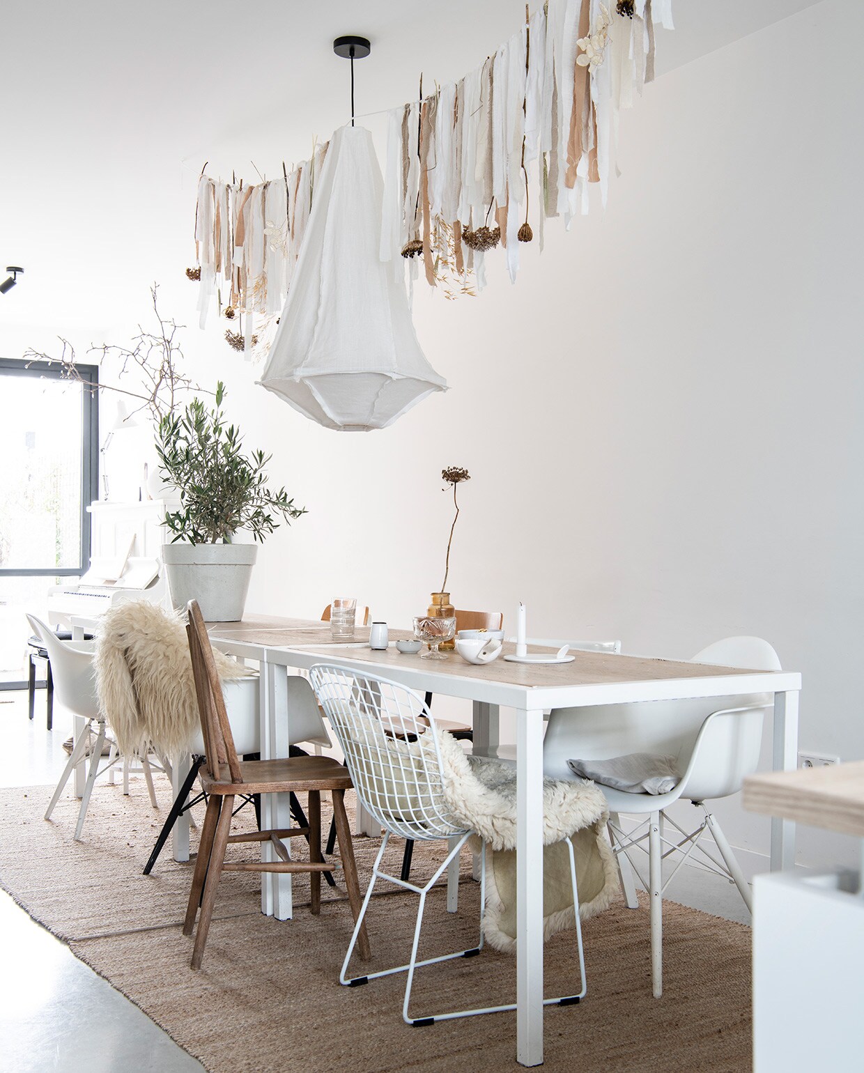 Tafels uit faillissementverkoop van een lunchroom. Draadstoel Jos Met Stijl, Eames-stoelen Loods 5, herkomst overige stoelen onbekend. Vachten op stoel en over leuning Vacht van Vilt. Kleden Wehkamp, hanglamp vtwonen, slinger Huize Jolie. Olijf in pot Budgetplant. Vaas kringloop Allerhande Panningen, kaarsenstandaard The Loving Wonen, schaaltjes, kommen en vaasjes Boet-Stijl.