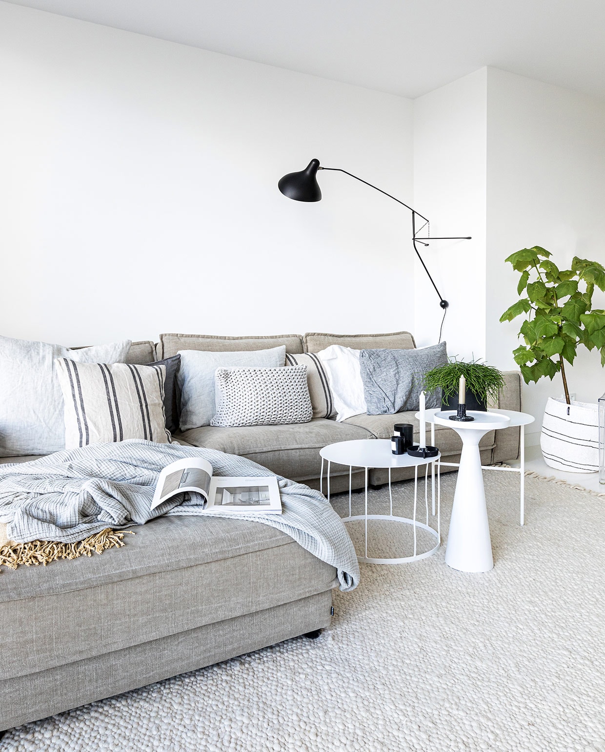 Muurverf Wijzonol ral 9016 (verkeerswit). Vloerkleed en bank Bolia. Kussens op bank Loft Loft. Grijze plaid Hay. Gele plaid H&amp;M Home. Bijzettafels, kandelaren K’willeminhuis. Bijzettafel met conische voet Zuiver. Geurkaarsen By Redo. Muurlamp DCW éditions. Bloempot Loods 5. Geweven mand Mifuko.