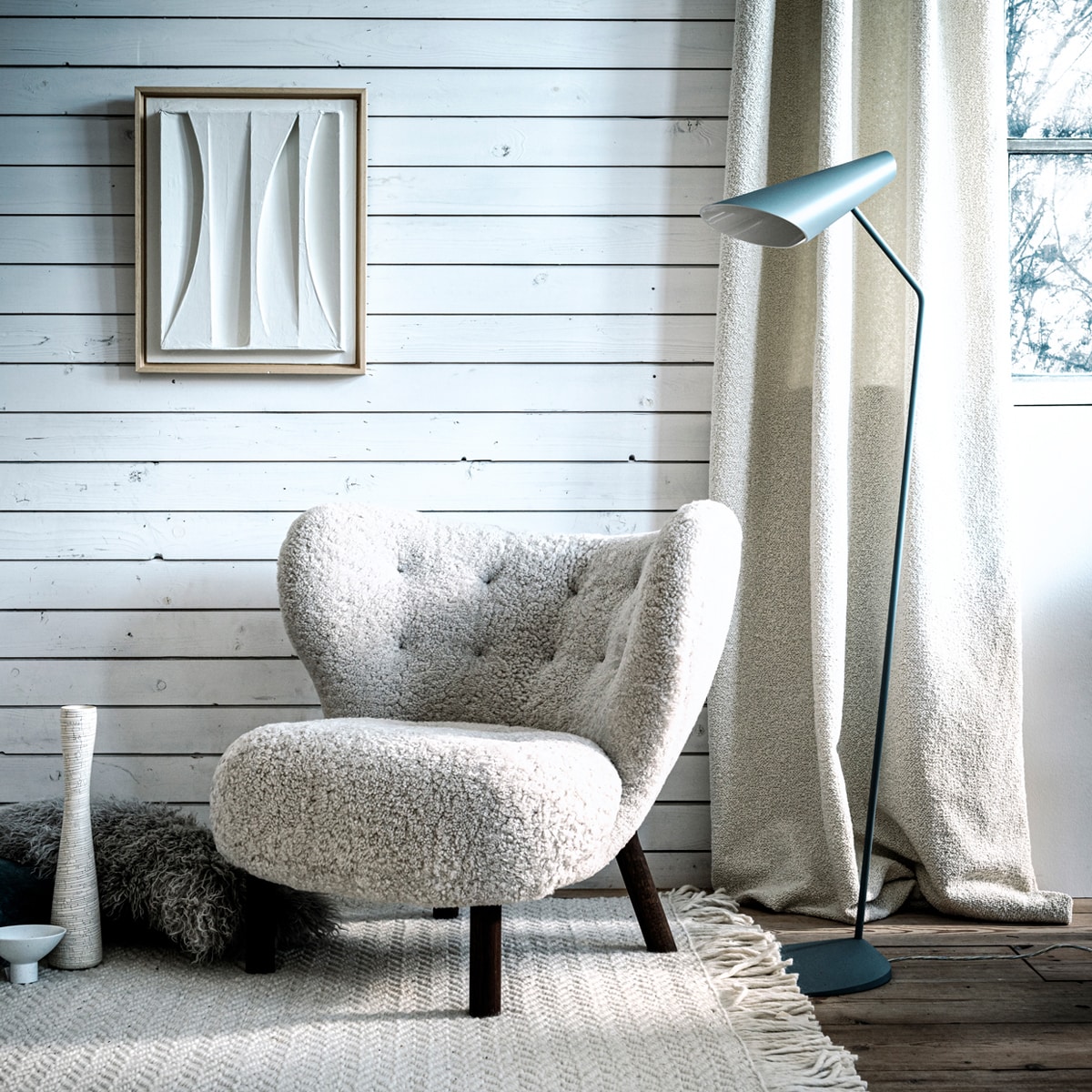 Witte fauteuil in bouclé stof (mobilia.nl). Vloerkleed (vtwonen.nl). Vloerlamp, 127×38 cm (hxb) (homestede.nl). Kunstwerk van Annemieke van Beek, als ruilobject (artinreturn.nl). Kussen (loods5.nl). Vaas met craquelé effect (covanderhorst.nl). Kom op pootje (hkliving.nl). Gordijnstof Frimas in kleur Ivoire van Nobilis (wva.nl).