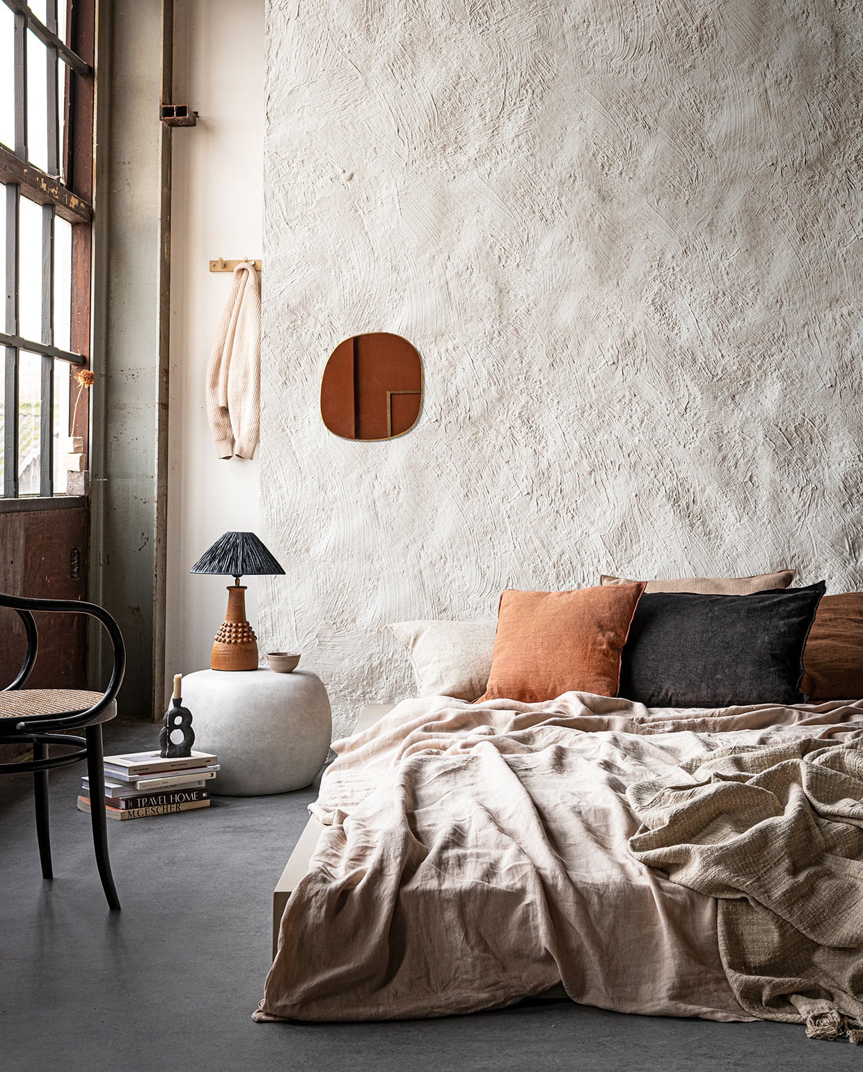 Muurverf in Chalk White (pure-original.nl). Bed op maat gemaakt en geverfd met Farrow &amp; Ball in Oxford Stone (com-anders.nl). Linnen dekbedovertrek in Sand van Linge Particulier, kussen Sabra offwhite Oblong XL, linnen kussenVice Versa van Maison de Vacances, kussen Vice Versa Canvas Formentera van Maison de Vacances, kussen Vice Versa Toile Nomade van Maison de Vacances, messing spiegel Ame van Caravane (couleurlocale.eu). Zwart kussen van vtwonen collectie (vtwonen.nl). Bijzettafel Pebble van vtwonen collectie (basiclabel.nl). Lamp van Madam Stoltz (deens.nl). Kandelaar van Malwina Kleparska, boek van Bea Mombaers (studio-yen.com). Kom van klei (household- hardware.nl). Kapstok van ByOn (littledreamers.nl). Stoel en overige boeken privébezit.