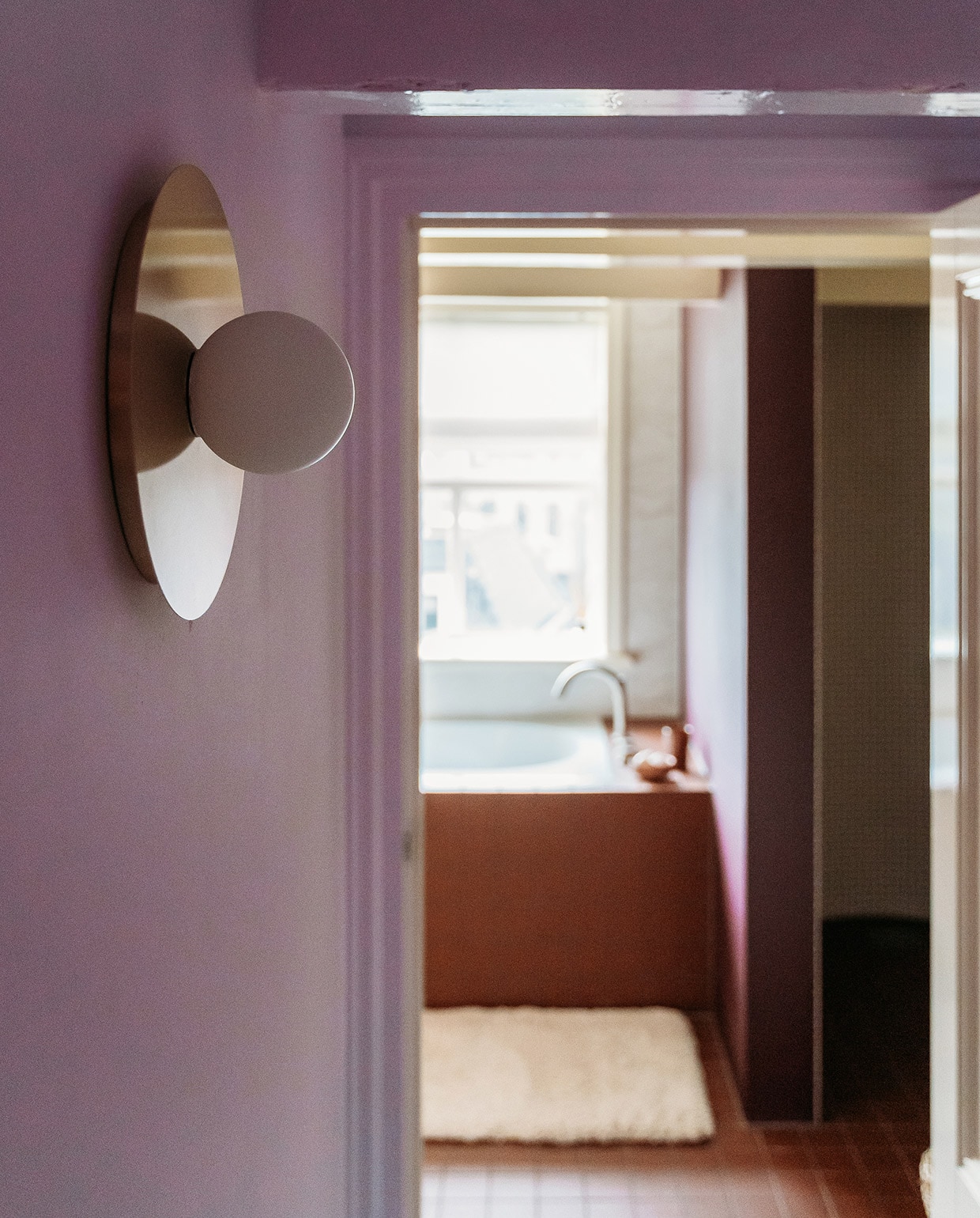 Lila muurverf GN 048-12 van Gamma, muurverf wand badkamer Brinjal van Farrow &amp; Ball. Wandlamp Starling van Westwing. Badmat Ikea. Tegels vloer en badombouw Vlak Rouge van Winckelmans.