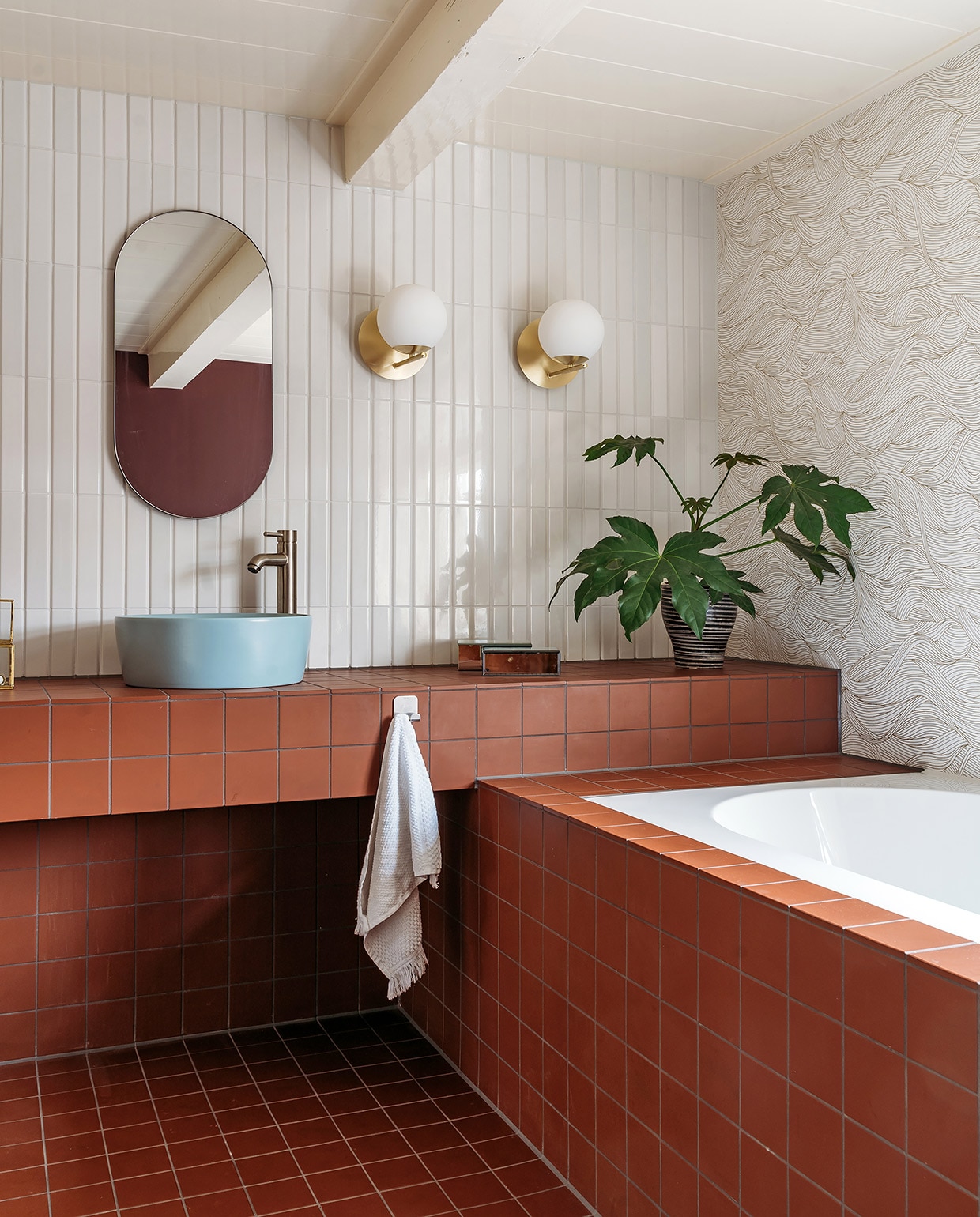 Tegels op vloer, wastafelmeubel en badombouw Vlak Rouge van Winckelmans, bovenste wandtegels Tinte Grigio Chiaro Lucido van Quintessenza. Wandlampen art deco van Flore via Lampenlicht.nl, spiegel House Doctor. Waskommen Stilo van Ben, kranen Cadans XL van Wiesbaden Sanitair. Spiegelbakje Zara Home, plantenpot kringloop. Behang Blossom Alula van Casamance. Kim heeft het twee keer met decorateursvernis van Polyvine behandeld.