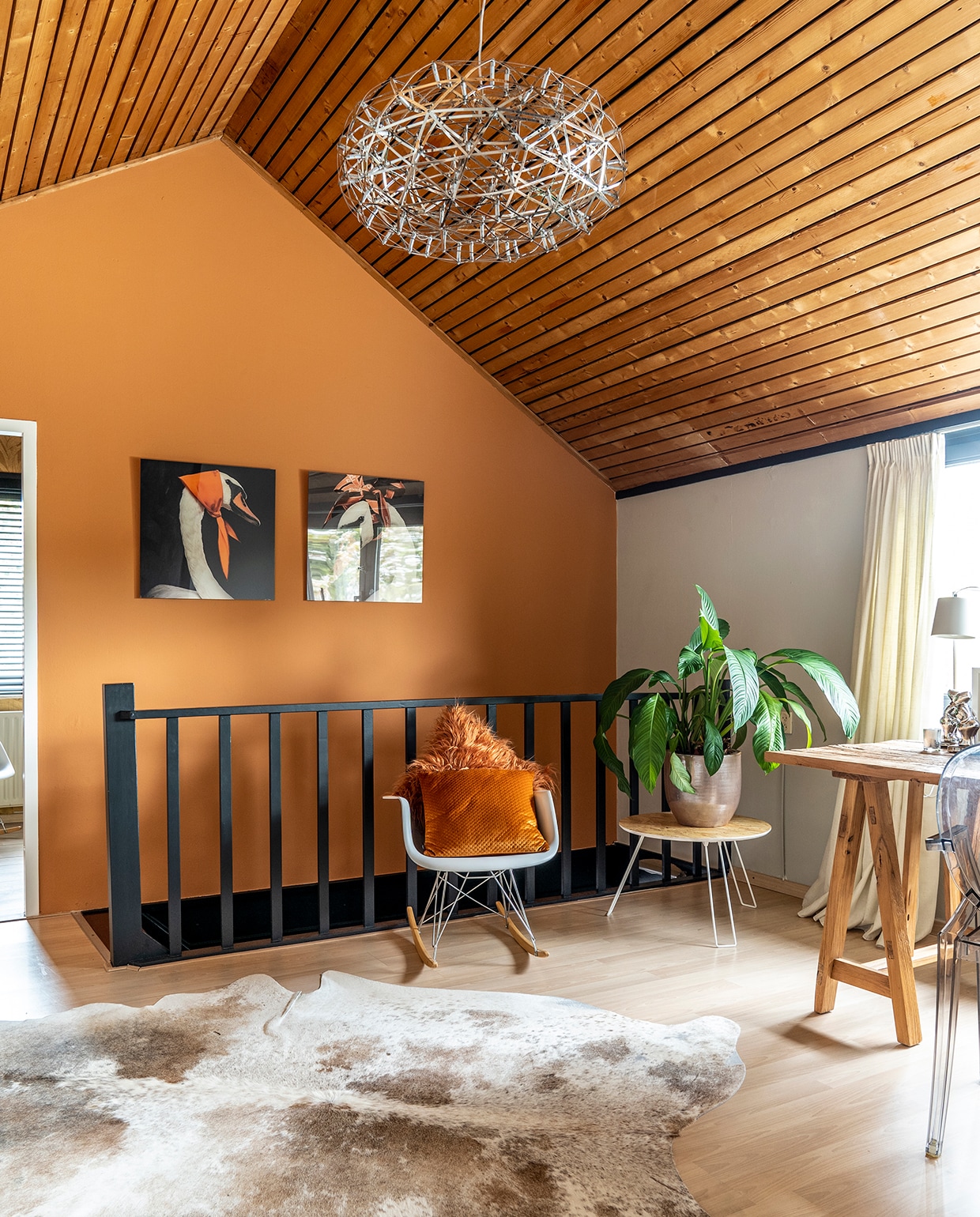 Op de overloop op de bovenverdieping een Eames schommelstoel (Vitra). Bijzettafel Zuiver, bureau LifeStyle. De hanglamp is geen echte van Raimond Puts, maar lijkt geïnspireerd op zijn ontwerp voor Moooi. Koeienvel Ebru, kunst Nicole Ponjée, verf Heat 24 van Little Greene.
