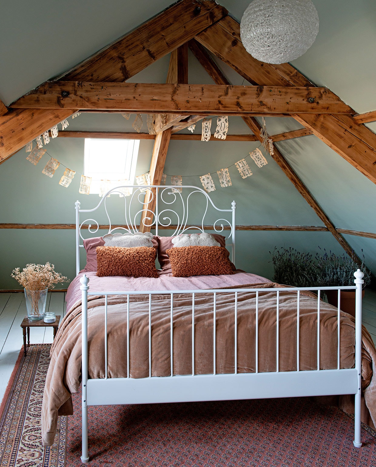 Muurverf Vert de Terre van Farrow &amp; Ball. Witte lak op vloer Action. Slinger zelfgemaakt van oude boeken. Hanglamp Kwantum. Bed Ikea. Lakens Jysk. Nachtkastje, vloerkleed en beige kussens kringloopwinkel. Vaas gekregen. Bloemen zelf gedroogd. Geurkaars Sissy-Boy. Terracotta kussens Jysk. Plaid H272984&amp;M Home. Lavendel uit de tuin van familie. Potten Tuincentrum Coppelmans.