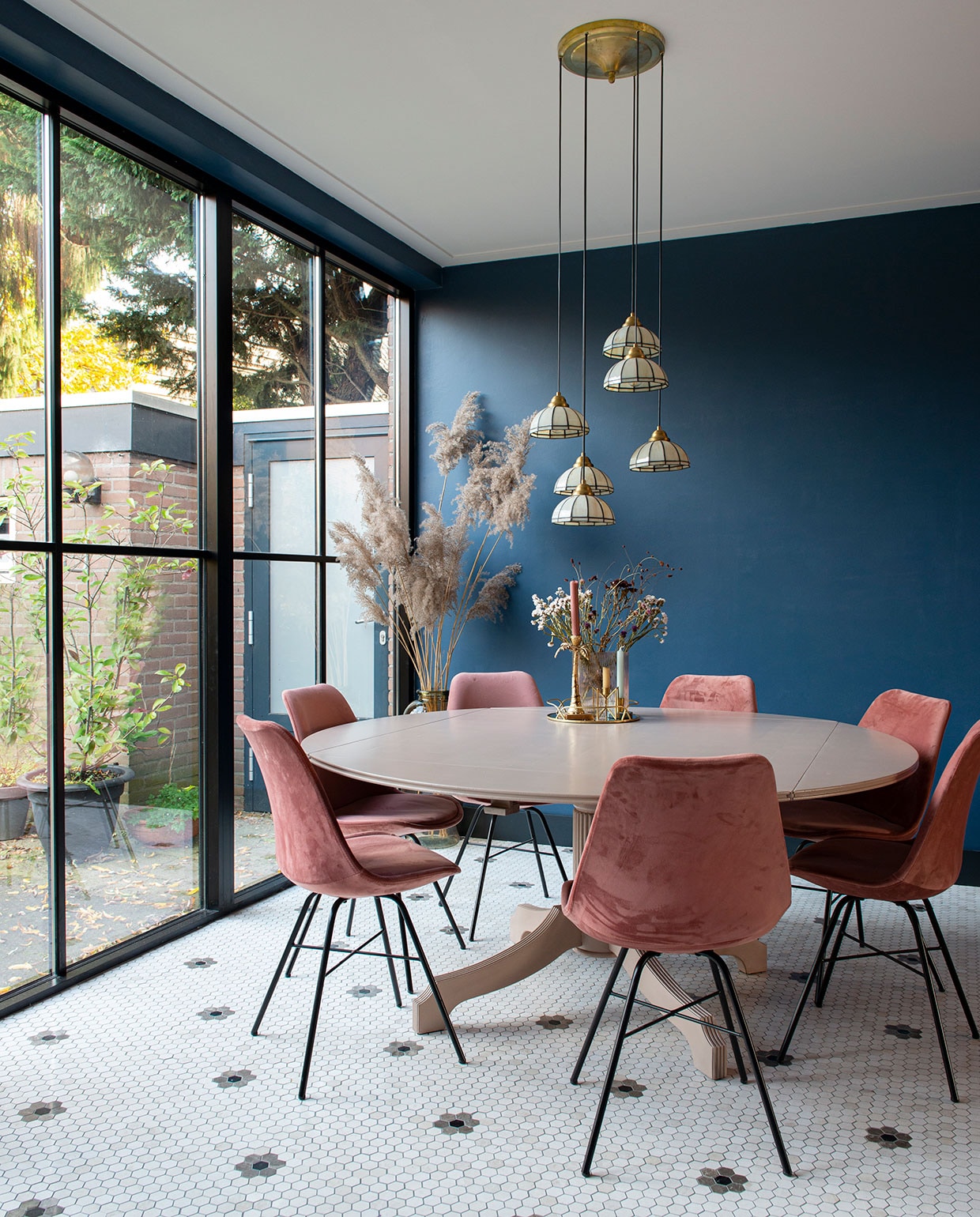 Tegelvloer Designtegels. Muurverf Stiffkey Blue van Farrow &amp; Ball. Plafondverf Slaked Lime van Little Greene. Eettafel kringloopwinkel, eetkamerstoelen Kick Collection. Hanglampen Marktplaats. Grote vaas Loods 5, pampasgras zelf geplukt. Kleine vaas Jysk, bloemen zelf gedroogd. Kandelaar palmboom gekregen, gouden kandelaars en spiegelplateau Sissy-Boy, borden kringloopwinkel, mokken gewonnen bij Designtegels.