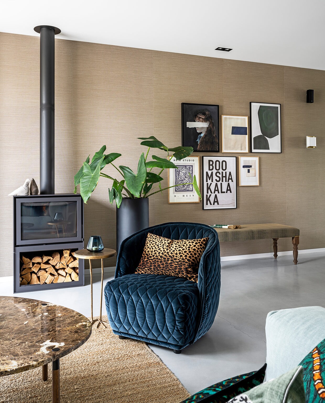 Behang Aztec Arte, houtkachel Barbas, zwarte plantenpot Micha Hulshof Bloembinder, bank La Vie Bohème met stof van Jim Thompson, fauteuil Redondo Moroso, panterkussen Mes, salontafel Bolia, bijzettafel Birdy Side Table Urban Outfitters, blauwe waxinelichthouder Prospectt, kunstwerken aan de muur van My Deer Art Shop en The Poster Club.