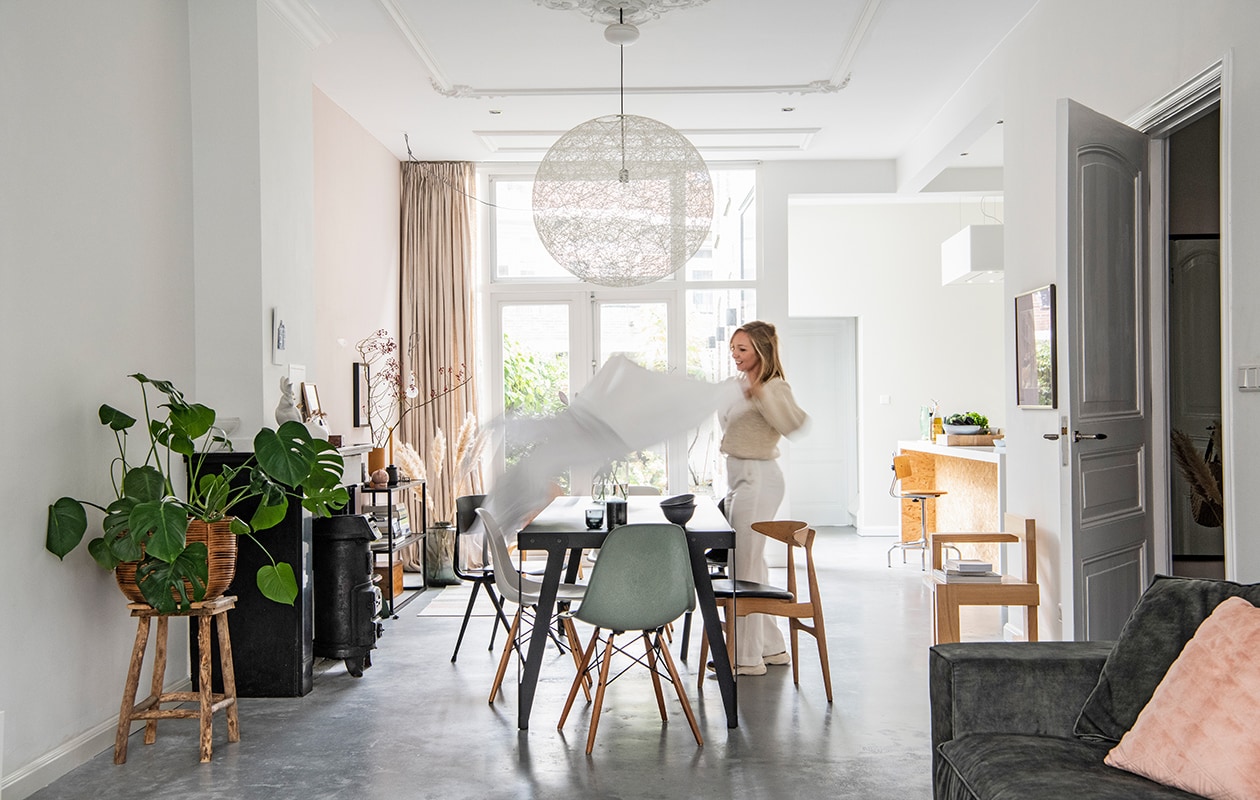 Muurverf links ral 9016, rechts E0.05.75 van . Tafel Lloyd en donkere houten stoel Wendela van Functionals, groene stoel DWS Eames van Vitra, zwarte stoel Revolt van Friso Kramer, houten stoel met zwarte zitting CH33 van Hans Wegner. Theepot Bredemeijer, mok en zwarte schaal Loods 5, vaas Bloomon. Hanglamp Random Light van Moooi. Houten stoel rechts gemaakt door Sanders vader, naar ontwerp van Gerrit Rietveld. Schilderij rechts Titus Meeuws. Keukeneiland Houtwerk, barkruk vintage, herkomst kraan onbekend, afzuigkap Zen van Novy. Bank Noelle van Room 108, kussen van HKliving. Planten-mand en kruk van tuincentrum.