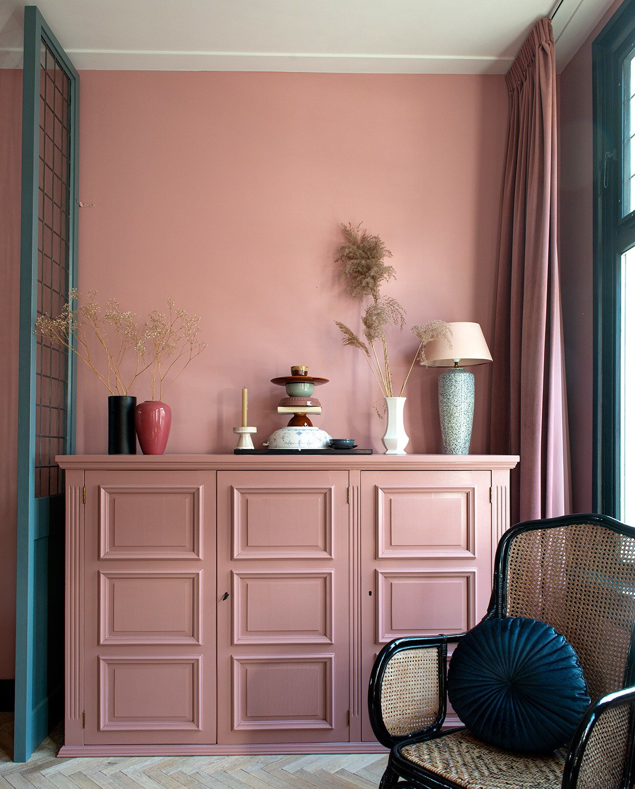 Muurverf Hellebore 275 van Little Greene. Visgraatvloer Loven Dageraad Vloeren. Panelen zelfgemaakt, kleur panelen De Nimes van Farrow &amp; Ball. Glas-in-lood Glasatelier Gielen. Kunstboom Brouwer &amp; Bien, pot Intratuin. Hanglamp Sissy-Boy. Kandelaar Søstrene Grene, gestapelde schalen en borden tweedehands. Gordijnen Leen Bakker. Vazen, schemerlamp, zwarte stoel en kast kringloop-winkel. Verf kast Blush van Little Greene. Blauw kussen Jysk. Pampasgras zelf geplukt.