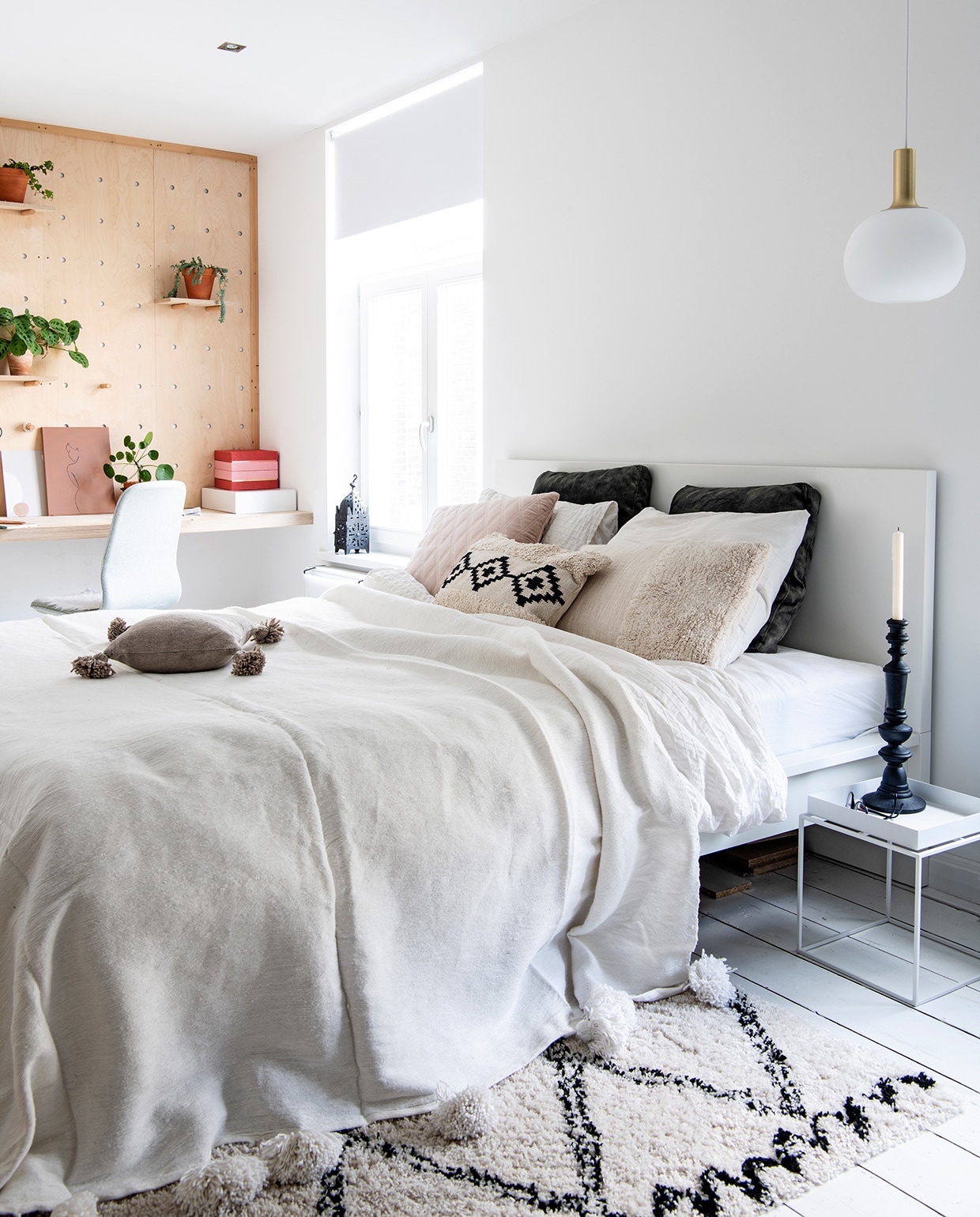 Pegboard en planken zelfgemaakt, accessoires op planken voornamelijk gekregen van ouders en grootouders. Vloerkleed Karwei, planten tuincentrum, bed en bureaustoel Ikea. Sprei El Ramla Hamra, hanglamp Nordlux, nachtkastje Hay. Herkomst overige onbekend.