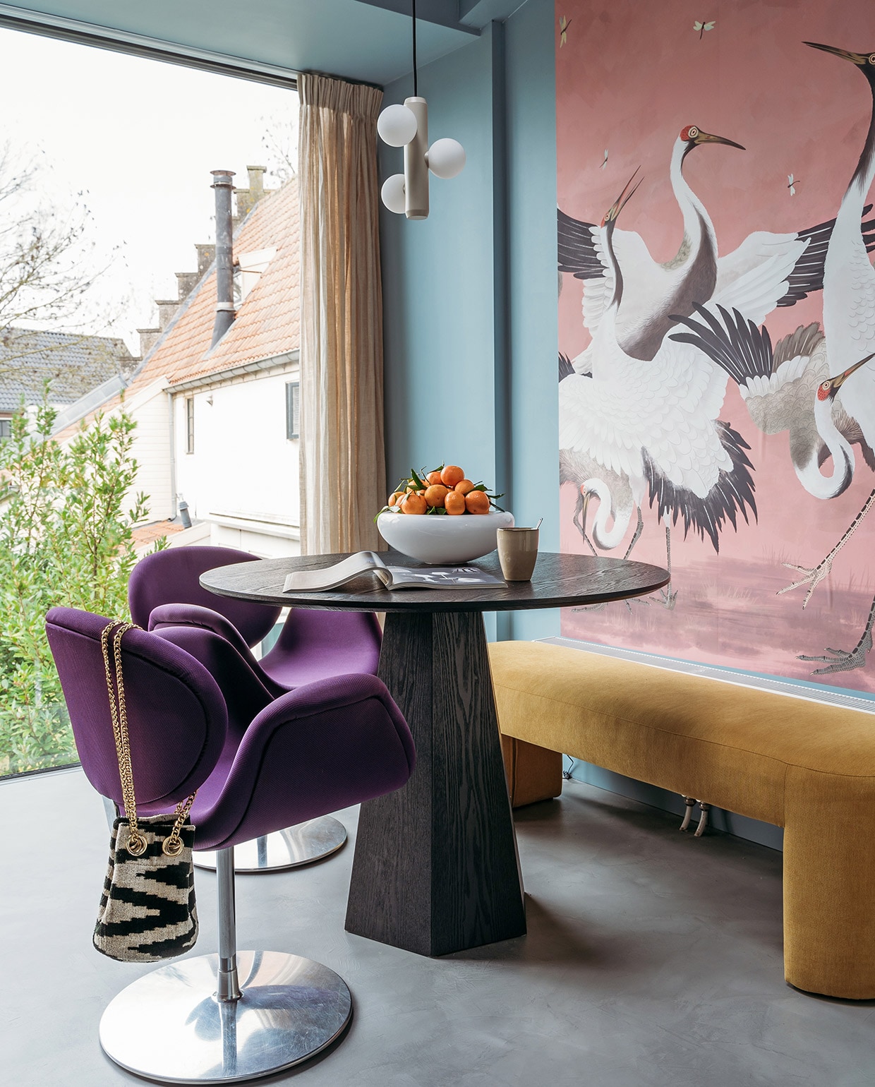 Verf muur en plafond R0.10.60 van Sikkens. Herkomst linnen gordijnen onbekend. Behang Heron Removable Peel and Stick Mural van AmsterdamElement. Tafel Pilar van Zuiver. Bank Lobby Bench van HKliving. Stoelen Little Tulip van Artifort via Marktplaats. Fruitschaal Eva Solo. Schaal Smiley van Tools Design. Beker Xenos. Hanglamp Kaktee van Fést. Tas Rough Studios. Vloer Cem-Line Micro van Loos Betonvloeren.