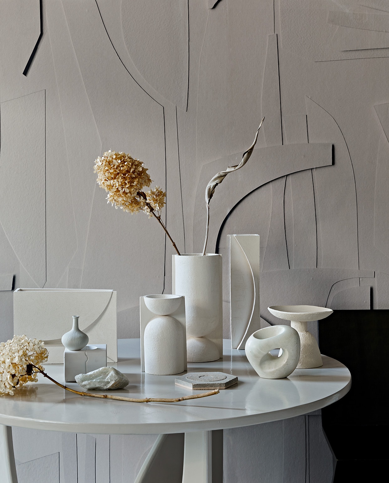 De serie vazen The Sand van witte chamotte klei kwam tot stand door een samenwerking van drie creatieven van Art in Return, Studio Yen en By Joa Amsterdam. Links smalle vaas Sun € 125,-, in het midden ronde vazen The Sand per 2 € 330,-, rechts rechthoekige vaas Moon € 230,- (, artinreturn.nl, byjoa.nl). Rechtsvoor sculptuur van speksteen € 350,- (lisetteleegwater.nl). Schaal keramiek op voet Moon Totem van Marlies Huybs € 300,- (studio-yen.com). Kleine porseleinen vaas € 21,95 (). Ronde tafel 120×75 cm (Øxh) vanaf € 750,- (com-anders.nl). Behang White Spirit, prijs op aanvraag, wordt op maat geprint (pascale-risbourg.com). Gedroogde hortensia’s en strelitzia (edenique.nl). Gietvorm in gips, stuk speksteen links vooraan (keramikos.nl).