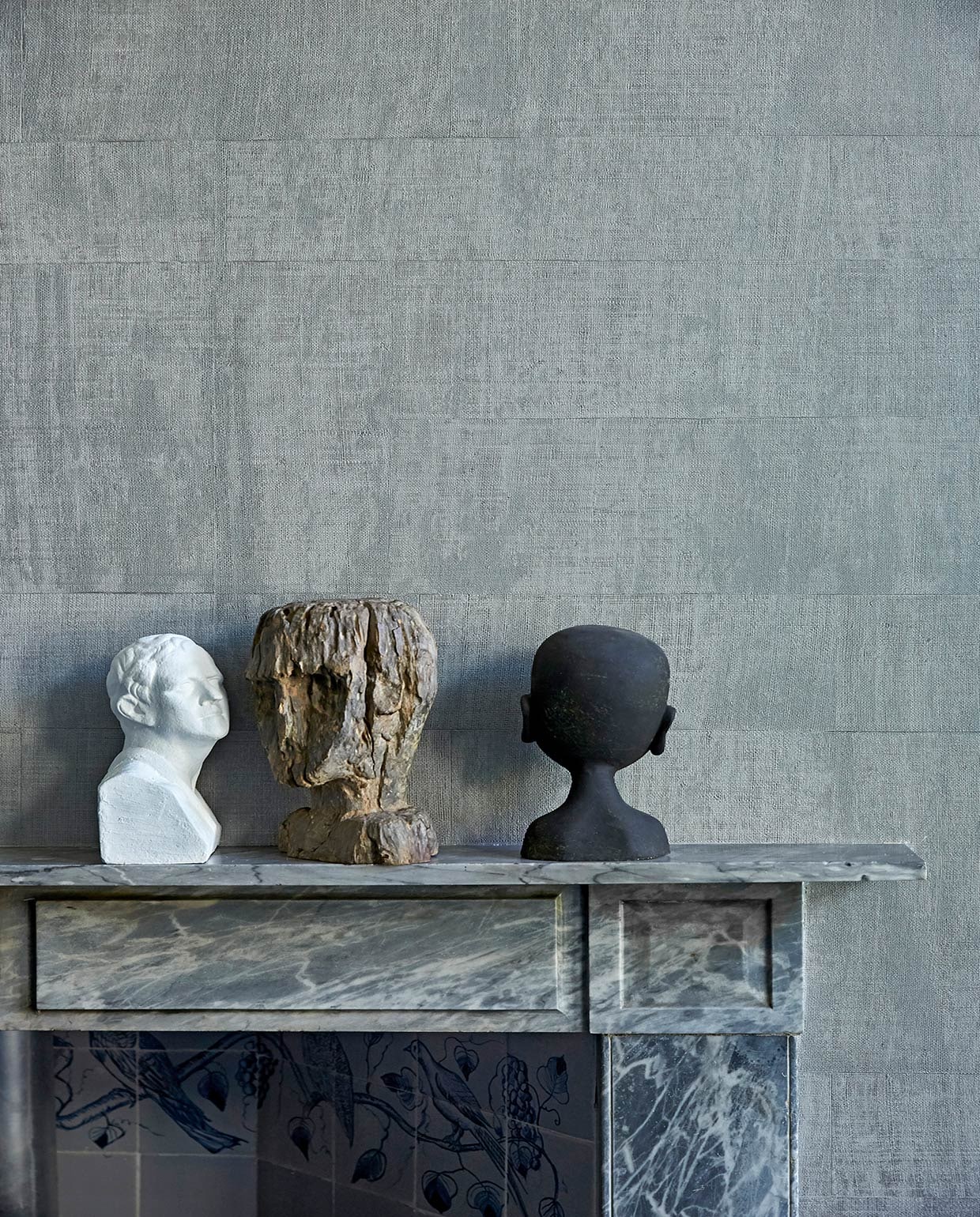 Grijs behang op muur Atelier d’Artiste Elitis via Loggere Wilpower. Marmeren schouw originele Rococo-schouw. Witte buste van een winkel die niet meer bestaat, antieke houten buste uit India, zwart hoofd van GMC uit Zuid-Afrika.