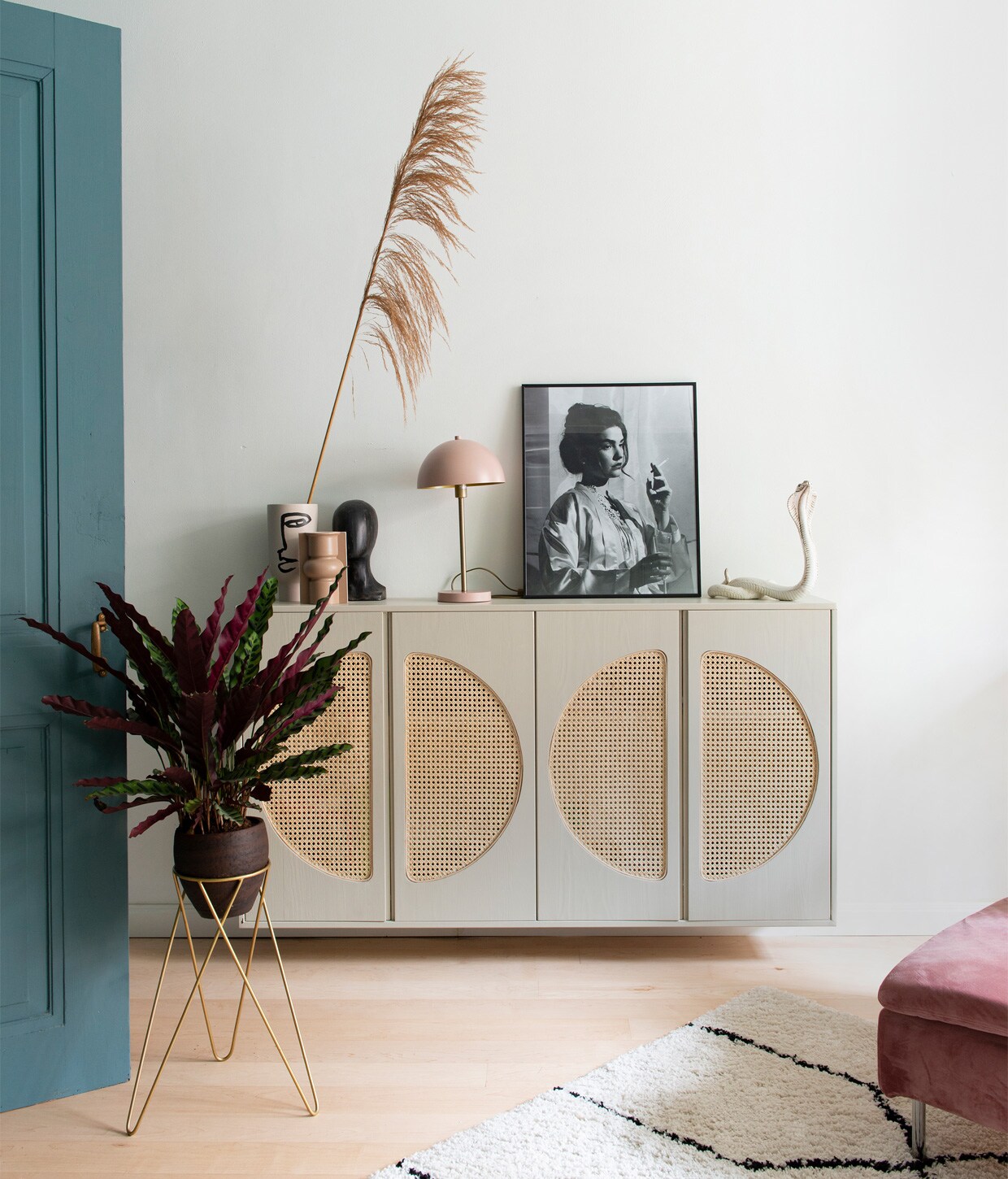 Kast Ivar van Ikea, zelf cirkels uitgefreesd en met pitriet omgebouwd tot webbingkast, geverfd met Drop Cloth van Farrow &amp; Ball. Vaas gezicht H&amp;M Home, voorste vaas en object gezicht HKliving. Lamp Rietveld Licht. Portretfoto van buurjongen gekregen. Beeld cobra vintage vondst. Plantenstandaard Sissy-Boy, plant Calathea. Vloerkleed Karwei, bankhoes Norsemaison. Verf deur Inchyra Blue van Farrow &amp; Ball, muurverf verkeerswit Ral 9016.