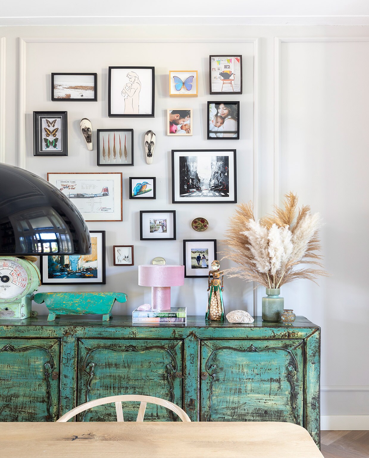 Dressoir uit Indonesië via Bij Jasmijn, tafel zwaartafelen.nl, stoelen Wishbone Chairs van Carl Hansen. Op dressoir: kleine pot Dekatuin, oude scheepsklok en groen houten kunstwerk uit Bali, roze lamp Westwing, Indonesische pop kringloop, vaas Made, minivaas van Christians oma geweest. Aan muur: fotolijsten Ikea en kringloop, maskers uit Zuid-Afrika, vlinders Anna + Nina en All the luck in the world, foto’s gemaakt door Natalia van der Zalm en Kee &amp; Kee, kunstwerken uit New York (vierkant), een atelier in Zwolle (ijsvogel) en cadeau gekregen.
