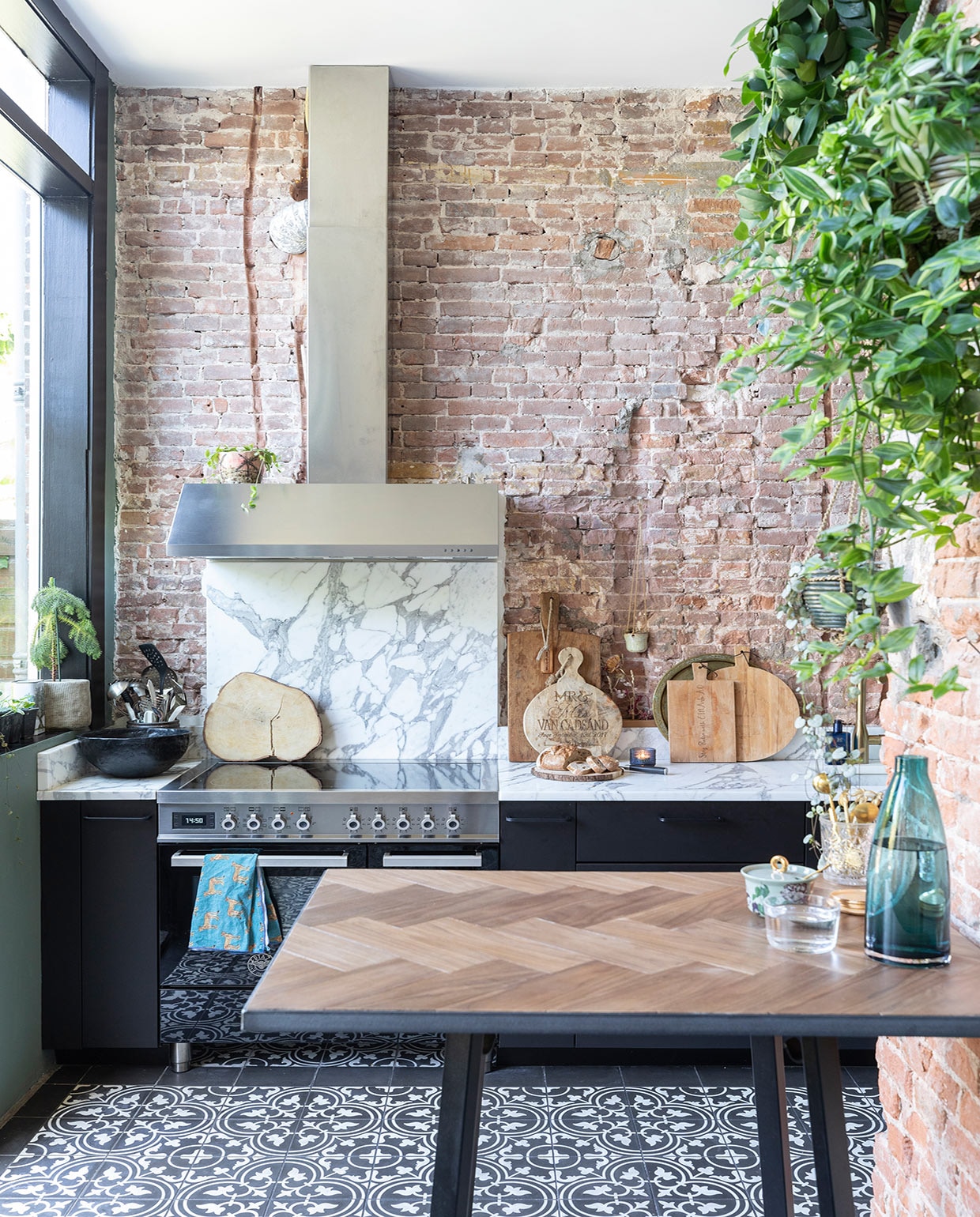Portugese vloertegels Designtegels, keukenkastjes Ikea, werkblad en spatwand van Carrara marmer door Swaalf uit Haarlem, fornuis Bertazzoni, groene muurverf Green Smoke en zwarte verf kozijnen Pitch Black Farrow &amp; Ball, pot in vensterbank, blauwe waterkan, waterglas en zwarte schaal Ikea, snijplank boomstam laten maken op Bali, snijplanken gekregen van vrienden, hangpot Dekatuin, pot op afzuigkap gekregen, hoge bartafel onderstel van Hay met massief eikenhouten blad gemaakt door SkillsXL, suikerpot van Essenza, vaas onbekend.