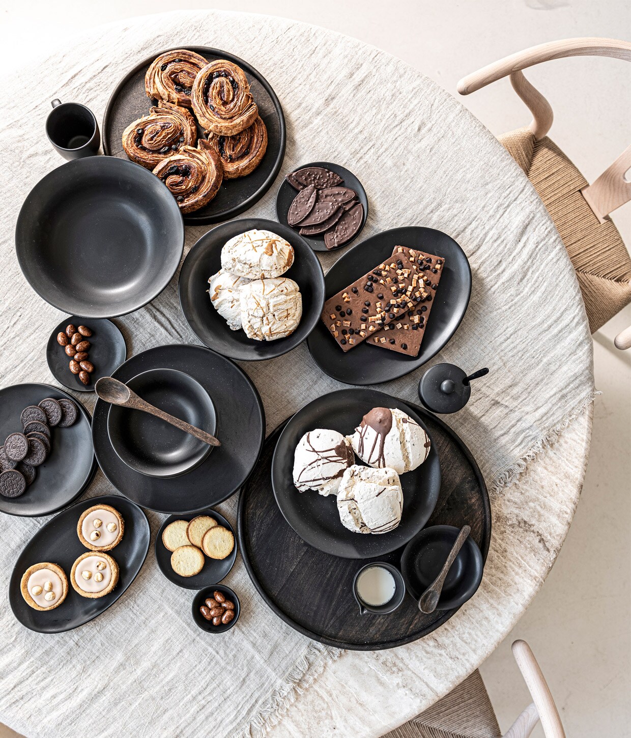 Mangohouten bord, 40 cm (Ø) € 49,95, ook in 50 cm (Ø) € 59,95, acaciahouten lepels, set van 2 € 10,95, zwart porseleinen servies,16-delig € 99,-, ook 36-delig € 239,- en los verkrijgbaar vanaf € 4,95,-, linnen tafelloper, 50×150 cm € 34,95, ook in donkergrijs en wit. M.m.v. pantoufle-design.nl (stoelen, tafel).