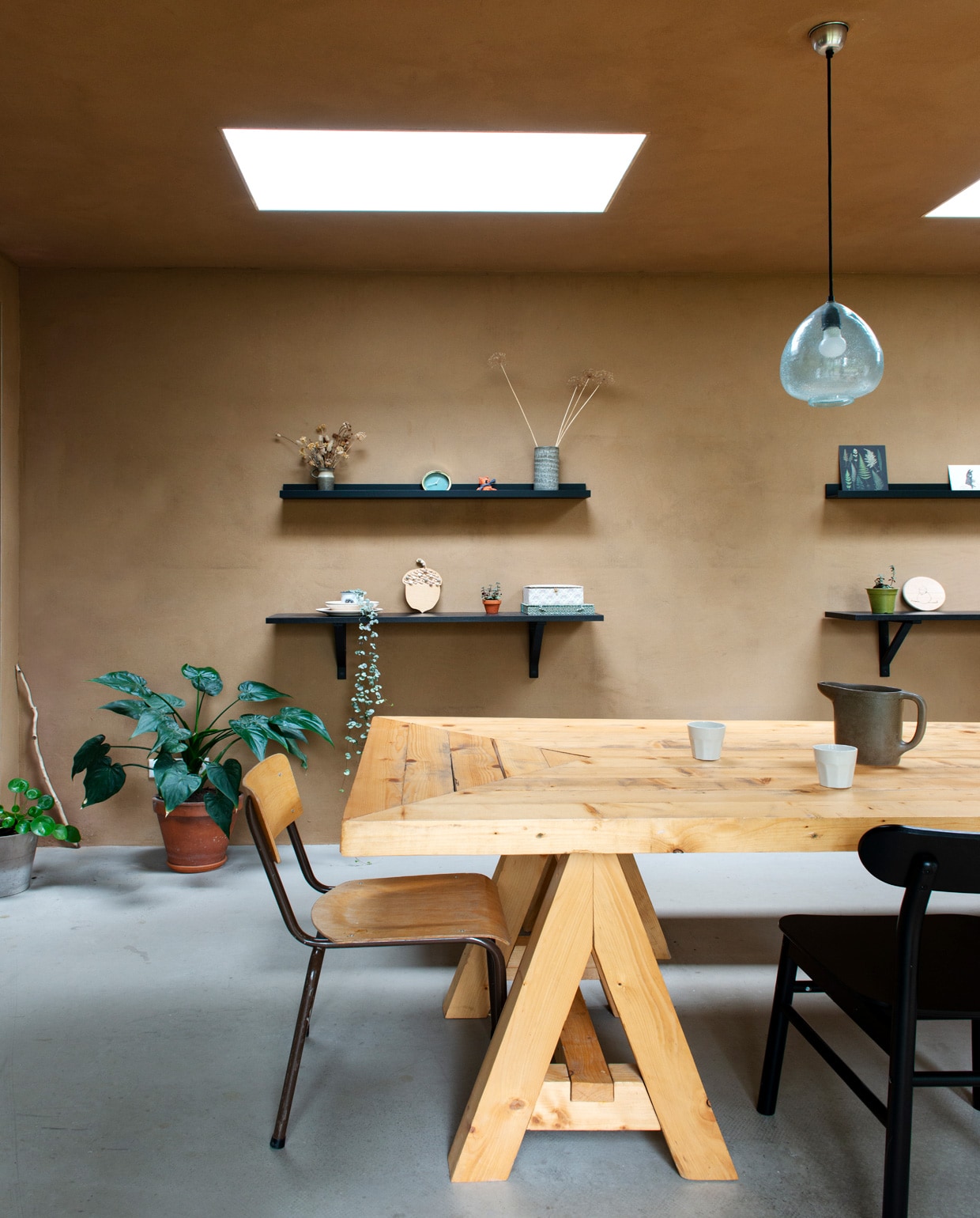 Wanden en plafond van onbehandeld leemstuc, vloer van beton. Muurplanken, vloerkleden, stoelen , hanglampen . Tafel en bank gemaakt door Joost. Vintage schoolstoel, schenkkan en vazen kringloop