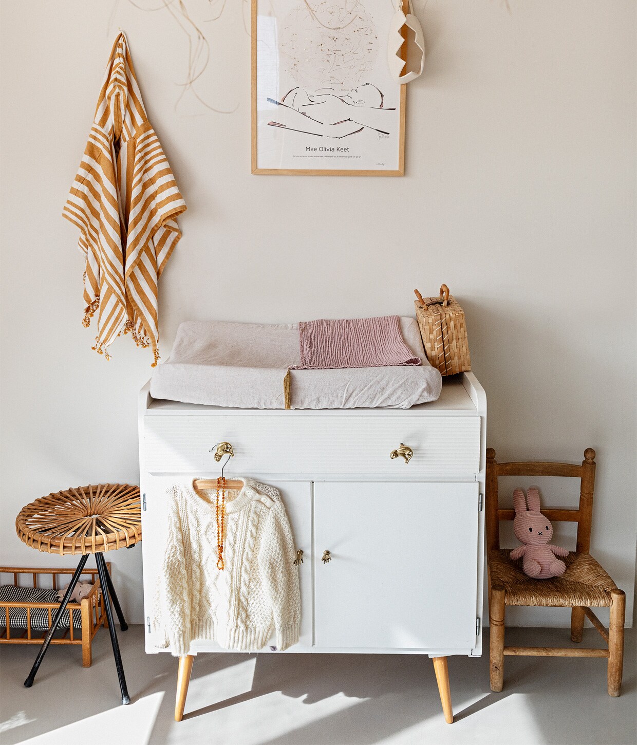 Muurverf Papyrus van Gamma, gietvloerNature Grey. Hanglamp Couleur Locale,kunst aan muur MrStarsky, strandponchokind Liewood. Vintage commodeMarktplaats, deurknoppen Doing Goods.Poppenbed en kruk van Dirk van Sliedregtvintage. Kinderstoel erfstuk Robertsfamilie. Rieten koffer kringloop, jutenkroon Suussies, naturel kroon en rozedeken Archive Store.