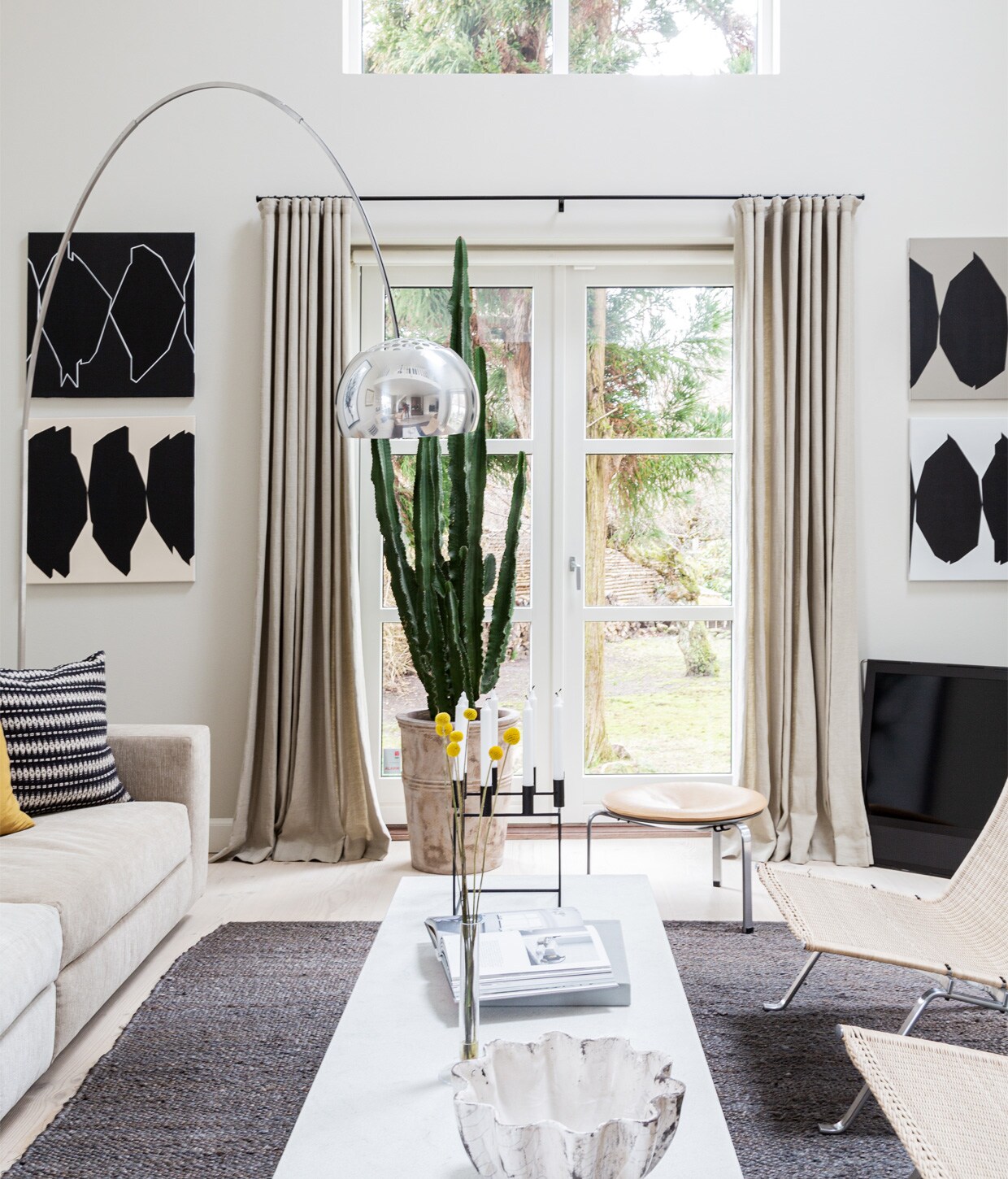 Muurverf Shaded White van Farrow &amp; Ball. Bank Eilersen. Kussens Tapet-Cafe. Koffietafel PK62 Poul Kjærholm voor Fritz Hansen. Lamp Arco van Flos. Kunstwerk in kleur Egill Jacobsen. Schilderij Cathrine Raben Davidsen. Vloerkleed Tine K Home. Kaarsenstandaard Mogens Lassen.
