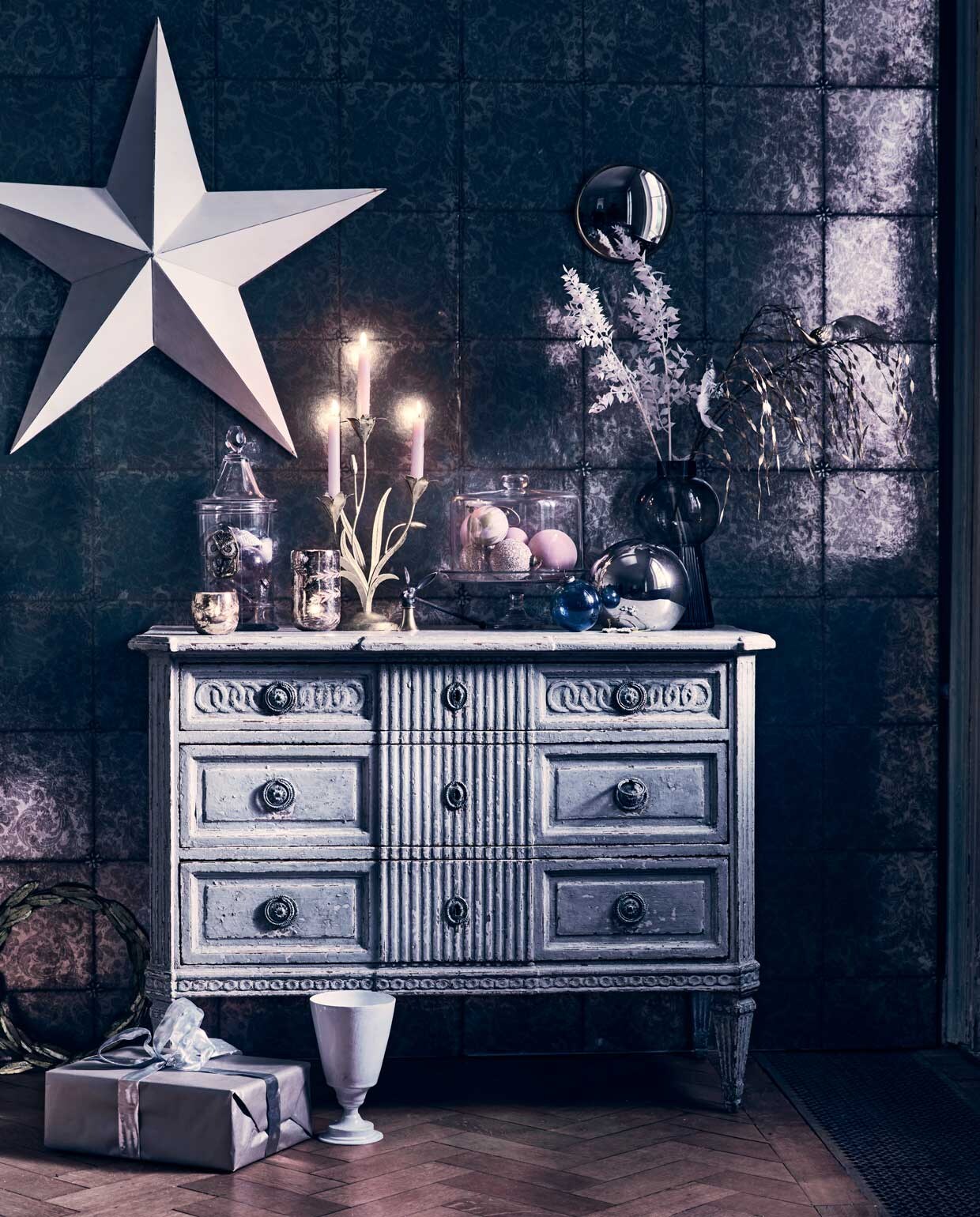 Behang Kings Mirror 98/13055 van Cole &amp; Son, rol 50 cmx10 m € 128,- (deruamsterdam). Antiek dressoir, prijs op aanvraag., glazen stolp met taartplateau € 295,-, voorraadpot met puntdeksel € 350,- (pietjonker.nl). Witte ster € 95,-, grote zilverkleurige waxinelichthouder € 19,50, kleine waxinelichthouder € 8,95, kleine ronde spiegel € 19,50 (weldaad.com). Kaarsendover € 39,95, witte vaas van Astier € 195,- (maisonnl.com). Roze glitterkerstballen € 4,50, gemarmerde roze kerstballen € 4,50 (nordal.eu), grijze glazen vaas van Bloomingville € 43,50 (vtwonen.nl). Zilveren glazen bal € 19,99 (hm.com). Grote transparante blauwe bal € 9,95, kleine kerstballen in voorraadpot vanaf € 1,95 (iblaursen.nl). Gouden krans van blaadjes € 51,99, gouden kandelaar € 30,- (bungalow.dk). Vogeldecoratie op tak € 14,99 (sissy-boy.com). Overig privébezit.