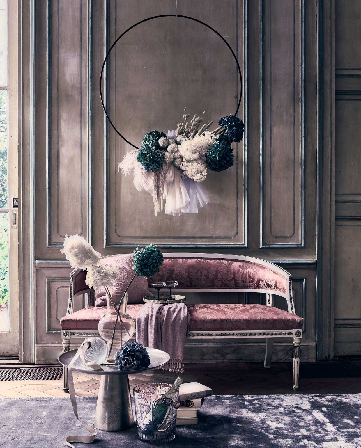Kerstkrans, op maat gemaakt door Edenique Floral Design, prijs op aanvraag (edenique.nl). Grijs vloerkleed Carter van Riverdale, 170×250 cm € 435,99, zilverkleurige bijzettafel Rune van Moos € 249,95, grijze champagnecoupes van &amp;klevering, set van 2 € 27,50, roze glazen vaas van &amp;klevering € 39,95 (vtwonen.nl). Glazen kerstbal € 9,75 (iblaursen.nl). Kristallen wijnkoeler, prijs op aanvraag (pietjonker.nl). Dienblad spiegel/goud € 24,99, roze chenille plaid € 19,99 (hm.com), roze fluwelen kussen, , 50×50 cm € 53,- (nordal.eu), antieke Franse bank € 950,- (prinsheerlijkantiek.nl). Overig privébezit.