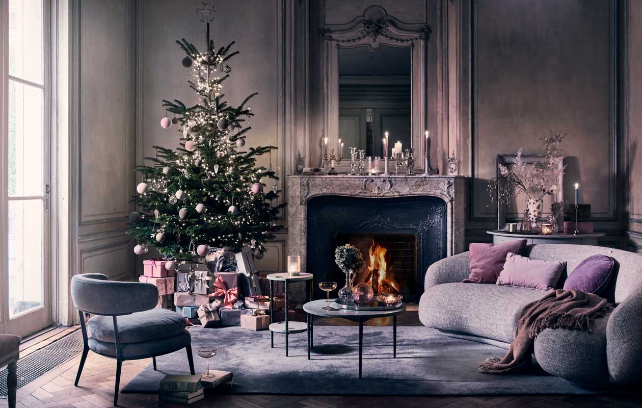 Kerstboom blauwspar (vanvulpenboomkwekerij.nl). Kerstverlichting vanaf € 29,95 (intratuin.nl). Vloerkleed The Moor AP7 in Blue Thunder van &amp;Tradition 200×300 cm € 2060,-, bank Juleo van Taccini in stof Equisetum € 5790,- (kasstoor.nl). Lichtgrijze fauteuil € 2502,- (edha-interieur.nl). Salontafel 77×40 cm (Øxh) € 595,-, bijzettafel met terrazzo-effect blad, 37×55 cm (Øxh) € 285,- (polspotten.nl). Grijze antieke halfronde sidetable, set van 2 € 1250,-, antieke tweearmige kandelaar, prijs op aanvraag, kristallen karaf met oor op salontafel en op de sidetable, vanaf € 60,- (prinsheerlijkantiek.nl). Roze fluwelen kussens, 50×50 cm € 48,- en 60×40 cm € 25,-, paars kussen, Ø 45 cm € 41,-, gedessineerde dozen met deksel, set van 2, vanaf € 45,-, glazen kom op tafel, set van 2 € 30,- (bungalow.dk). Roze cocktailglazen € 10,67, roze glazen karaf € 39,99, roze en okergele kerstballen in fluweellook € 4,-, roze glitterkerstballen € 4,50, gemarmerde roze kerstballen € 4,50, glazen windlicht op bijzettafel € 30,- en op schouw € 40,-, grote glazen kaarsenstandaard € 141,50, roze suède dozen, set van 3 € 106,60 (nordal.eu). Glazen pegelvormige kersthangers € 4,95, gouden vogels € 3,50, gouden vleugels € 3,50, gouden glittersterren vanaf € 12,50, stervormige piek € 12,50, goudkleurige kerstboomhanger € 4,50, glazen ballen met netje vanaf € 4,95, ballen met facetten vanaf € 3,95 (weldaad.com). Antieke zilveren armeluiskandelaars vanaf € 150,- (pietjonker.nl). Plaid € 45,- (maisonnl.com). Keramieken kandelaar € 17,99, goudkleurige kandelaar € 9,99, zilverkleurig dienblad op salontafel € 24,99 (hm.com). Grote glazen lila kerstbal € 9,75 (iblaursen.nl). Wit met goud gedessineerde vaas van Jonathan Adler € 589,- (luxerybynature.nl). Overig privébezit., ,