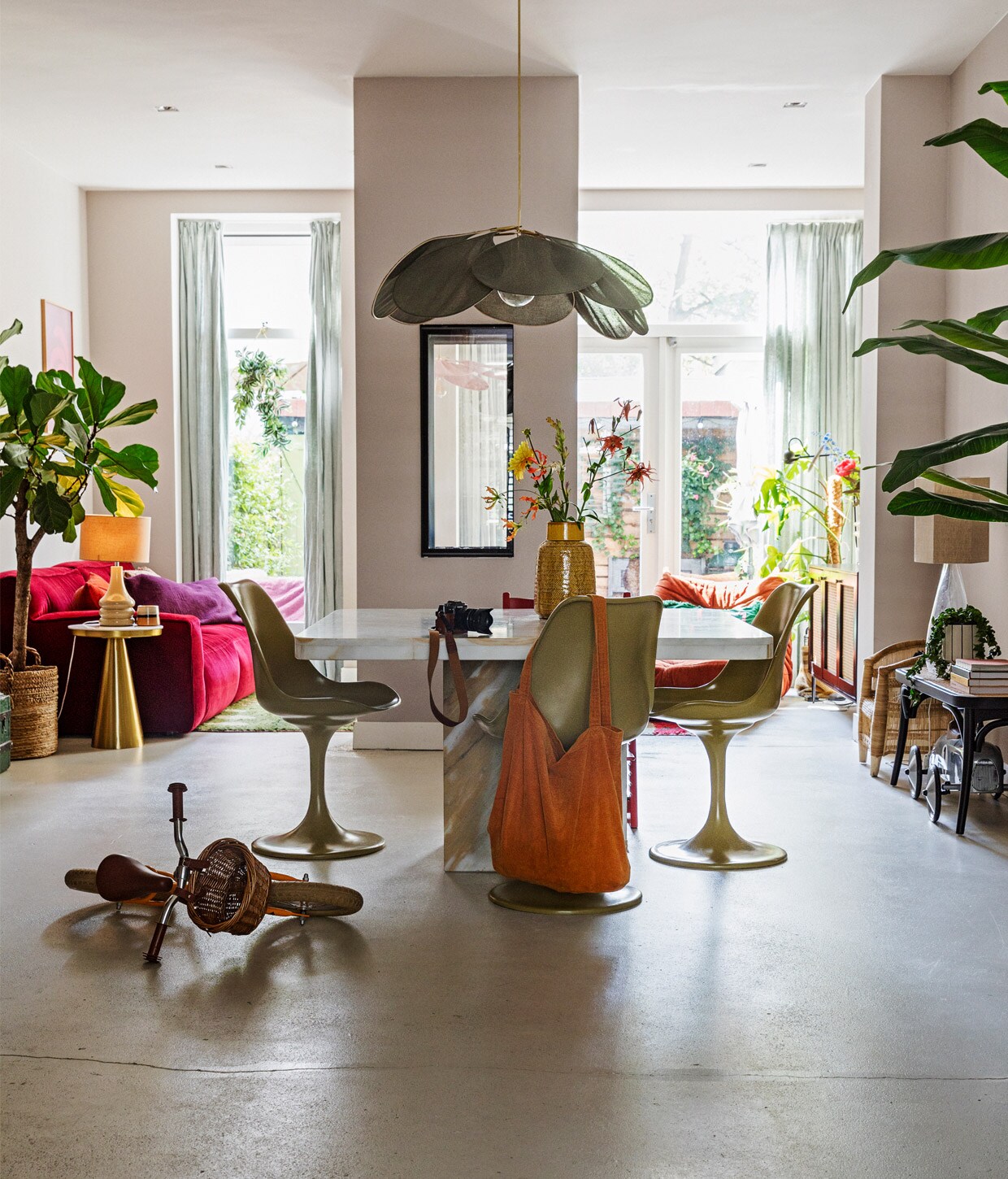 Muurverf Poedergrijs, mengkleur van Praxis. Wijnrode bank Clay van Fest Amsterdam, kunstwerk boven bank Enkel Art Studio. Plant en mand Green Stories, bijzettafel, tafellamp en dressoir Westwing, mok en langwerpige vaas HKliving, paars kussen Madam Stoltz via Deens, oranje kussen via De Weldaad in Amsterdam. Groen vloerkleed The Souks, oranje fauteuil Ligne Roset Togo opnieuw bekleed met stof van de Noordermarkt. Tafel Marktplaats, eetkamerstoelen Casa Gitane, gele vaas Leen Bakker, groene hanglamp Rockett St George, rieten kinderstoel Archive Store. Raambekleding Kwantum, fiets Veloretti.