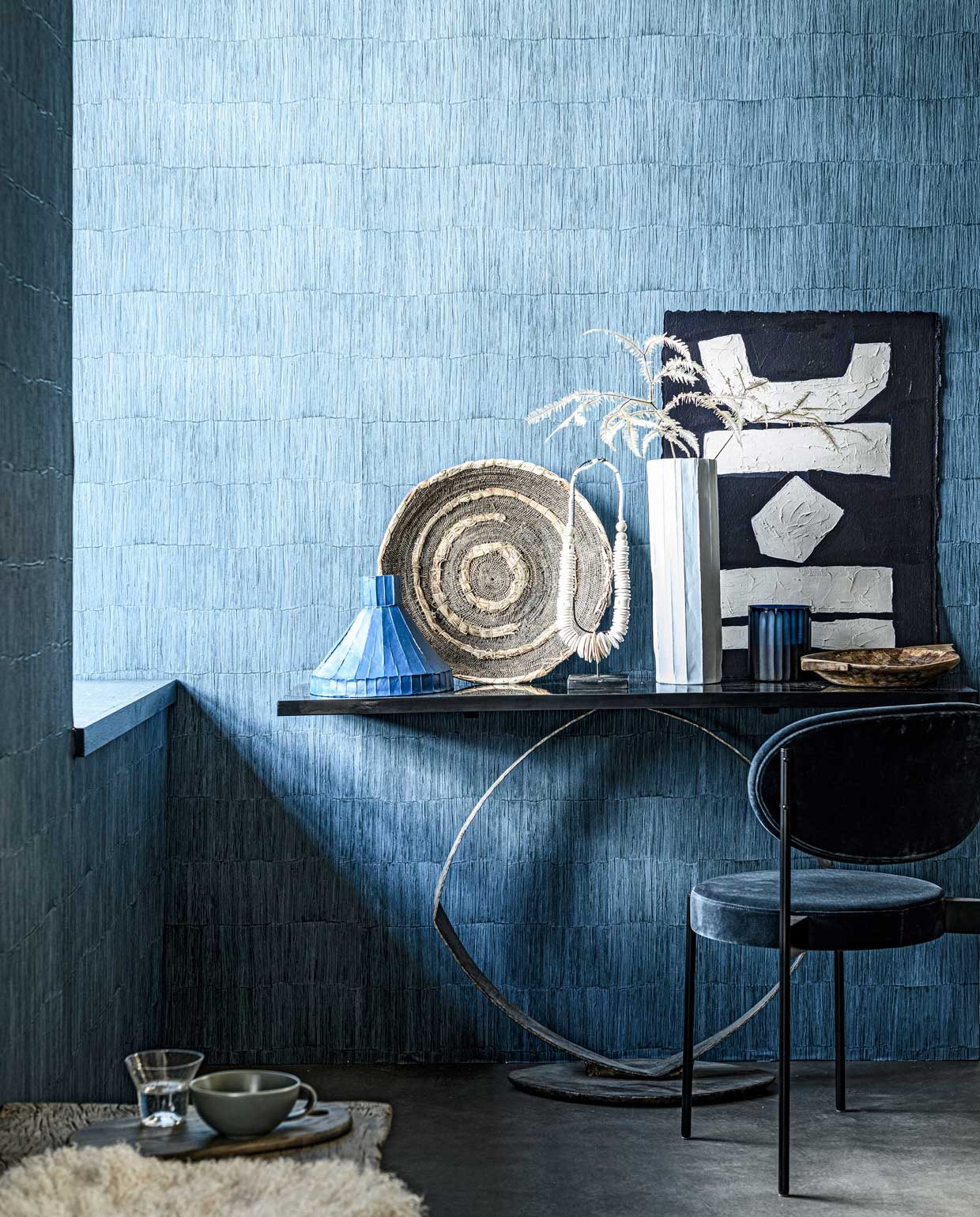 Behang Sakiori Ink uit de Casablanca-collectie van Designers Guild, rol 70 cm x 10 m € 117,- (wva.nl). Sidetable, 135x38x80 cm (lxdxh) prijs op aanvraag, geurkaars in blauw glas € 115,- (covanderhorst.nl). Oude geweven Makenge mand € 137,50 (couleurlocale.eu). Blauwe keramieken vaas € 232,50, witte keramieken vaas € 169,- (badenbaden.nl). Ketting op voet € 85,95, oude houten schaal € 27,50 (loods5.nl). Kunstwerk uit The Heritage Series, prijs op aanvraag (irisdorine.com). Stoel € 780,- (kasstoor.nl). Houten snijplank, per 2 € 79,- (fermliving.com). Glas van Serax, per 4 € 32,99 (vtwonen.nl). Mok € 9,- (paviljoennoord.com). Schapenvacht € 99,- (studio-yen.com).