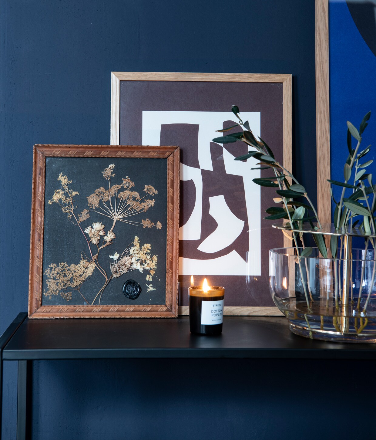 Zwarte kast Woood, poster abcd van The Poster Club, vierkante poster Object Blanc van Atelier Cph, ingelijste droogbloemen van een vriend gekregen. Vaas Ikebana van Fritz Hansen, kaars Royalty Scented van Tom Dixon.