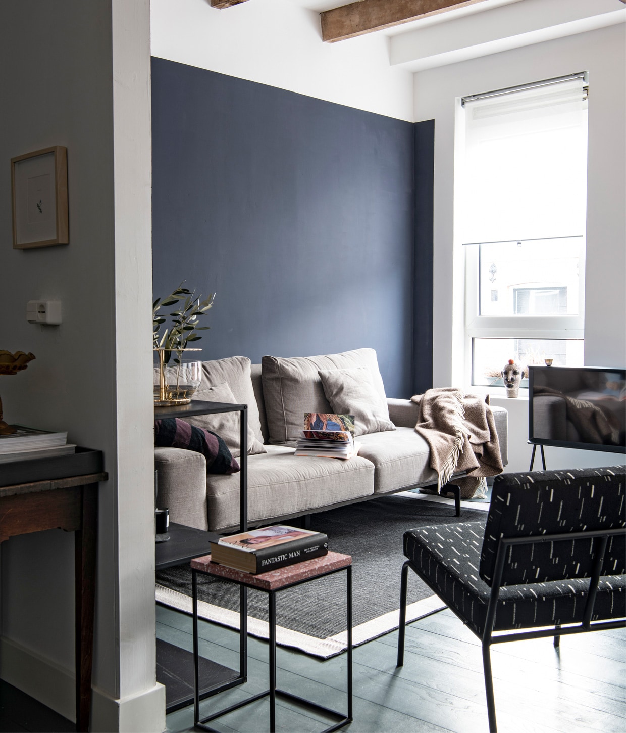 Muurverf Majestic Cloth van Pure &amp; Original, vloerverf Down Pipe van Farrow &amp; Ball. Bank Zico van Passe Partout, vloerkleed Bougari. Televisie Serif donkerblauw Samsung, stoel Monday Lounge van Fest Amsterdam. Bijzettafel via Loods5, kast Woood.