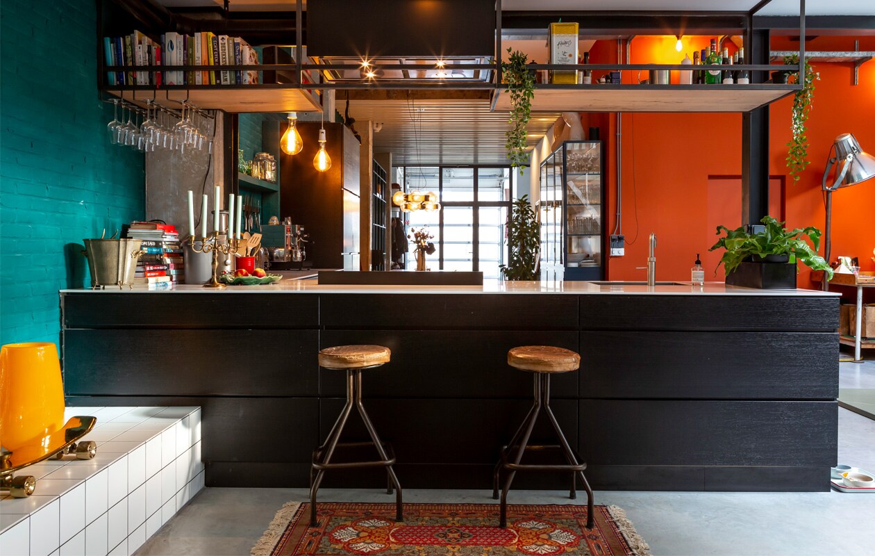 Keuken van Kvik met wit kunststof blad en zwarte frontjes met voelbare houtstructuur. Rek boven de bar gemaakt door Special Metal in Alkmaar. Theepot met koperen schild Bredemeijer, koffiemachine Buscaglione. Keramieken schaaltjes gemaakt door Marieke, Marokkaans glaswerk uit Marrakech. Hanglampen gemaakt van oude bakelieten fittingen met led-lampen.