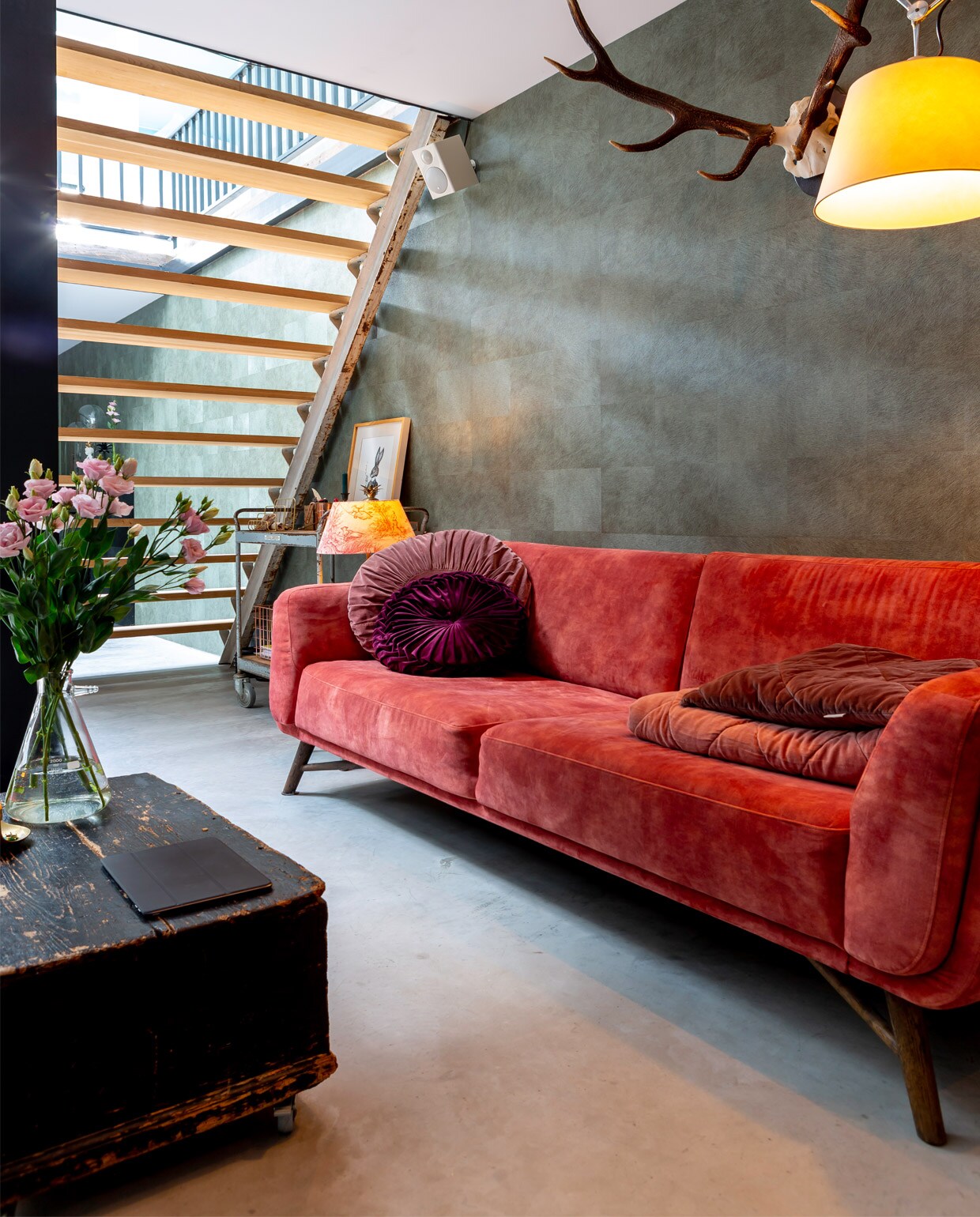 Bank en ronde kussens Decor Amsterdam, plaid Sissy Boy. Harig behang in vierkanten-patroon van Elitis, vloerlamp Tolomeo Mega Terra van Artemide. Gewei, ziekenhuistrolly en krukje gekocht in de Kloosterstraat in Antwerpen. Kist op wielen uit een antiekloods in Gent. Lamp Leentje Engelen, kap Van Dijk &amp; Ko.