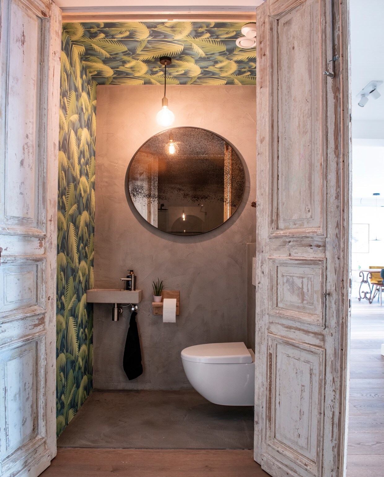 In het toilet werden muur én plafond behangen met behang Palm Jungle van Cole &amp; Son via De Mooiste Muren. Wasbak en kraan Nijhof. Ronde spiegel Notre Monde. Lamp Tala. Toiletpapierhouder Pilat &amp; Pilat.