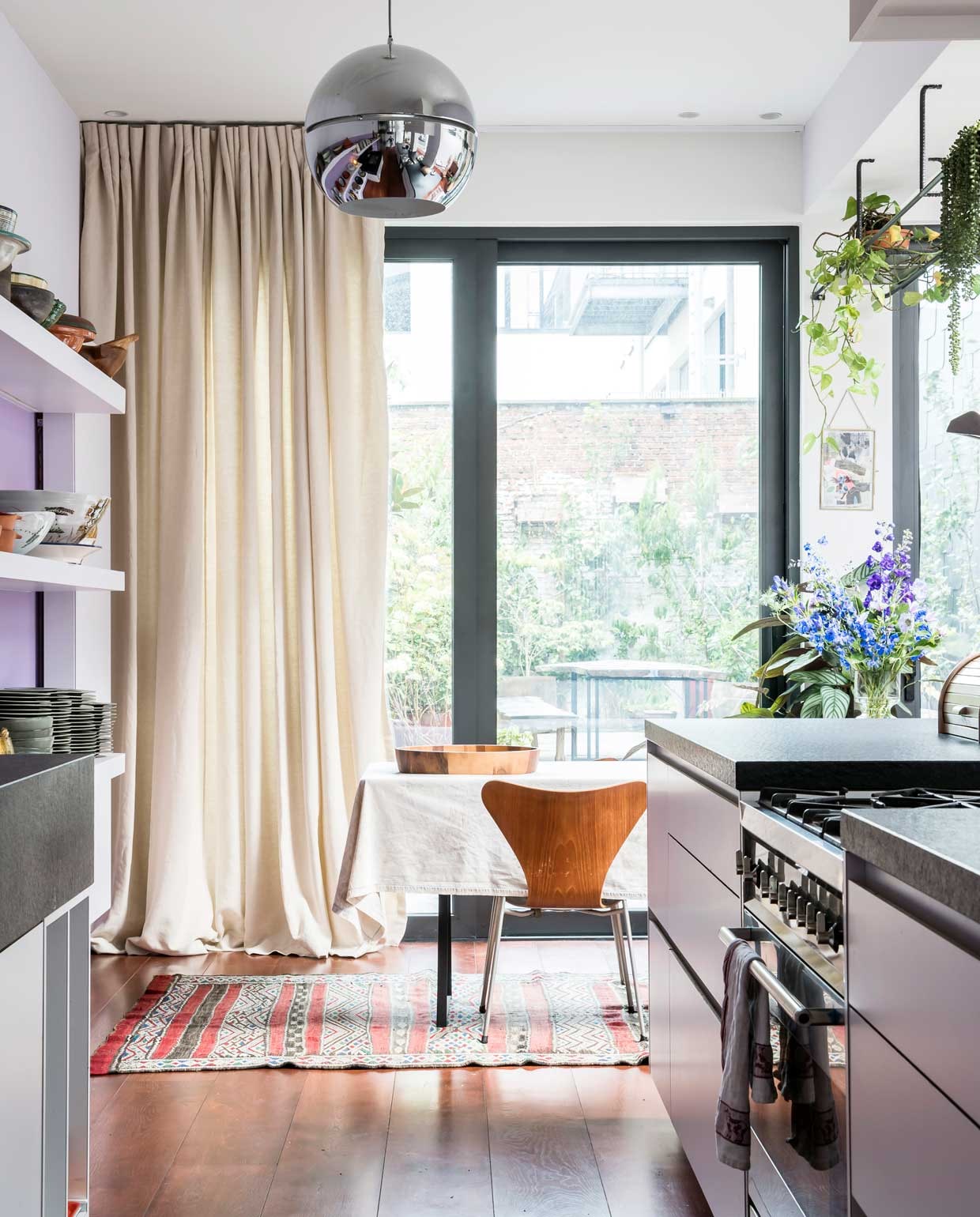 Aan het plafond hangen vintage bollampen in inox, gekocht in Brussel. De vlinderstoelen van Arne Jacobsen kocht Caroline bij Cornette de Saint Cyr, het gordijn is van Moodz.be, Alexandre De State is een gepassioneerd verkoper met sublieme stoffen. Het tapijt van is van Bazar Bizar, een winkel die nu is overgenomen.,