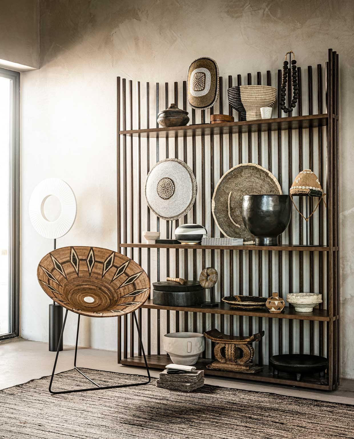 Houten kast € 4990,- (roche-bobois.com). Links staande lamp € 1099,-, zwarte grote pot in kast € 520,-, links ernaast gestreepte pot € 350,- (edha-interieur.nl). Kleed op de grond 250×350 cm € 1800,- (elitis.fr). Notitieboek op de grond per stuk € 29,95 (badenbaden.nl). Stoel Lalibu Hippie 75x47x90 cm (bxhxØ) , € 1490,-, mand op bovenste plank pedestal, 30×25 cm € 69,-, hoedje met schelpen uit Kameroen op staander € 420,-, witte graanpot van papiermaché rechts in kast € 49,-(couleurlocale.eu). Pot van hout, links op bovenste plank € 95,-, ernaast kralenschild € 249,-, zwarte ketting van glaskralen uit Ghana op bovenste plank € 109,-, wit rond schild uit Kameroen € 425,-, ronde gevlochten schaal in midden € 135,-, op de plank eronder kralenarmband op statief € 109,-, kleine mand ernaast € 109,-, houten krukje Ashanti op onderste plank € 375,- (o-live.nl). Zwart en wit mapje op grond, per stuk € 22,-, wit kopje op bovenste plank € 25,-, boek midden in kast € 65,- (sukha.nl). Ovalen kist op bovenste plank € 35,99, wit potje van aardewerk midden links € 9,99, witte pot van aardewerk met handvat onderin € 45,99 (zarahome.com). Overig bezit van de locatie (republiekbloemendaal.nl).