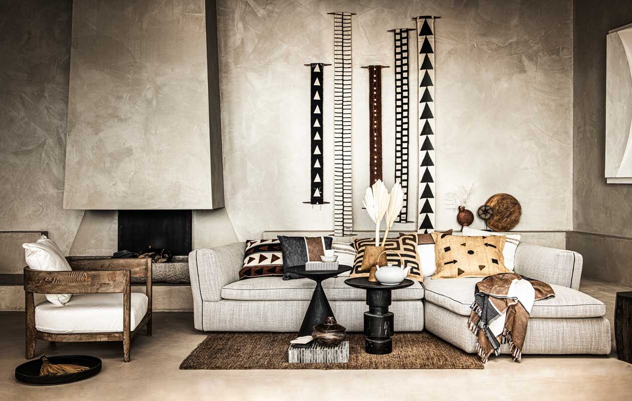 Loungestoel met houten frame € 950,- (nettydegroot.nl). Schaal op de grond € 95,-, bijzettafel links € 1799,-, vaas op bijzettafel rechts € 50,-, bruine vaas achteraan € 40,-, hoekbank € 11.330,- (edha-interieur.nl). Totem wandhanger vanaf € 79,-, kussen links op de bank € 199,-, theepot € 79,-, zwart en wit mapje op doos, per stuk € 22,-, wit kopje op tafel € 25,-, schaaltje op tafel € 30,-, boek € 65,- (sukha.nl). Kussen tweede van links, 50×50 cm € 39,95, kussen in het midden met zwarte tekening Unique Pieces vanaf € 220,-, kussen rechts ernaast 50×50 cm € 39,95, kussen met pijlen en stippen Unique Pieces vanaf € 220,-, plaid op de bank 130×200 cm € 129,95 (mlfabrics.nl). Kwast op schaal € 25,99 (zarahome.com). Doos op de grond € 247,11 (badenbaden.nl). Droogtakken prijs op aanvraag (waterdrinker.nl). Houten schaal tegen achterwand € 79,-, ecru kelimkussen met beige streep uit Turkije, 50×50 cm per stuk € 49,- (couleurlocale.eu). Houten ronde pot op de grond € 95,-, kralen armband op statief op achtergrond € 109,- (o-live.nl). Overig bezit van de locatie (republiekbloemendaal.nl).