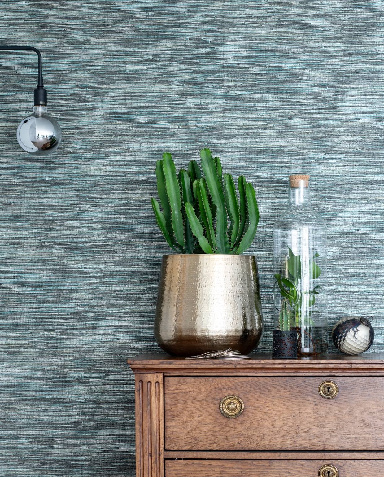 De houten ladekast is een erfstuk. Behang Anthology I Seri Slate via De Mooiste Muren. Goudkleurige bloempot en plant in vaas van Intratuin. Lamp van Menu.