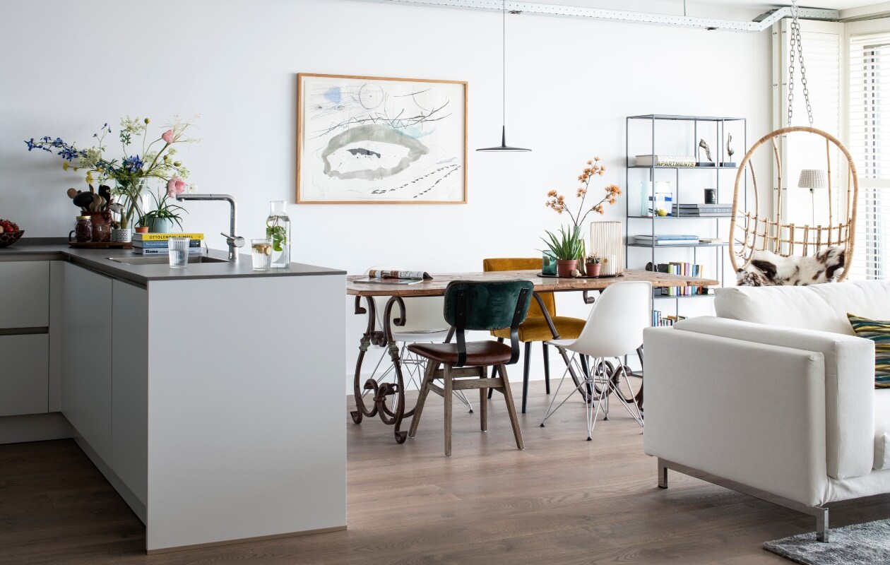De eettafel is een uniek stuk en niet meer verkrijgbaar. Hanglamp 0270 van Vibia Skan. Witte stoelen DSW van Eames via Vitra. Gele stoel van Woood gekocht bij Karwei. Groen-bruine stoel LifeStyle. Kunstwerk van Meria Bakker. Boekenkast Zuiver. Bank Ikea.
