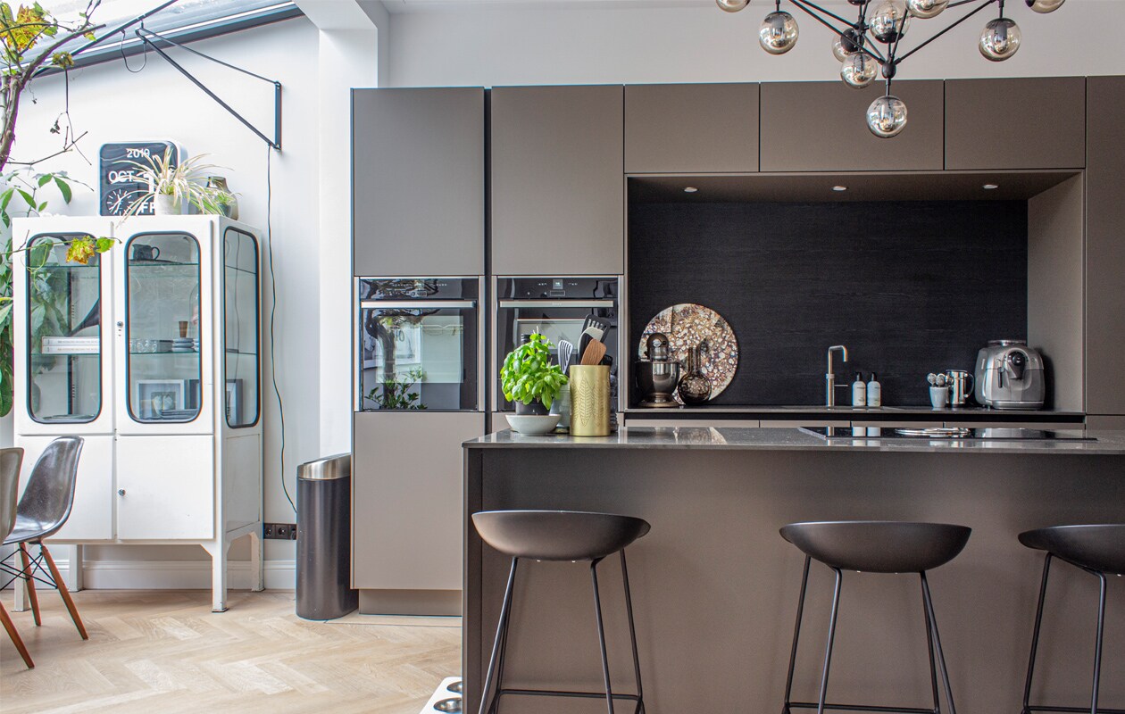 Apothekerskast wereldspul.nl, klok Vintagelab15, Stoelkuipjes marktplaats.nl en lovelyandco.co.uk, nieuwe onderstellen via designonderdelen.nl, Siematic-keuken in kleur Umbra in matte uitvoering met een blad van composiet. Lamp met rookglas Loftlamp. In de nis: bruine vaas Karwei, bruine karaf H&amp;M home, mokken van Broste Copenhagen. De stalen binnenpui is gemaakt door Brink Stalen Deuren. Prullenbak Brabantia. ,