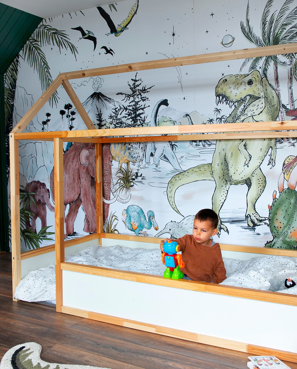 Dino-behang Annet Weelink Design, vloerkleed dino Ginger Roots. Dekbedovertrek Mies &amp; Co, bed met zelfgemaakt dak Ikea. Krat op wielen en houten vlaggenlijn Wibra. Mobile met origami-vogels handgemaakt kraamcadeau. Kledingrek gemaakt door Sofies vader