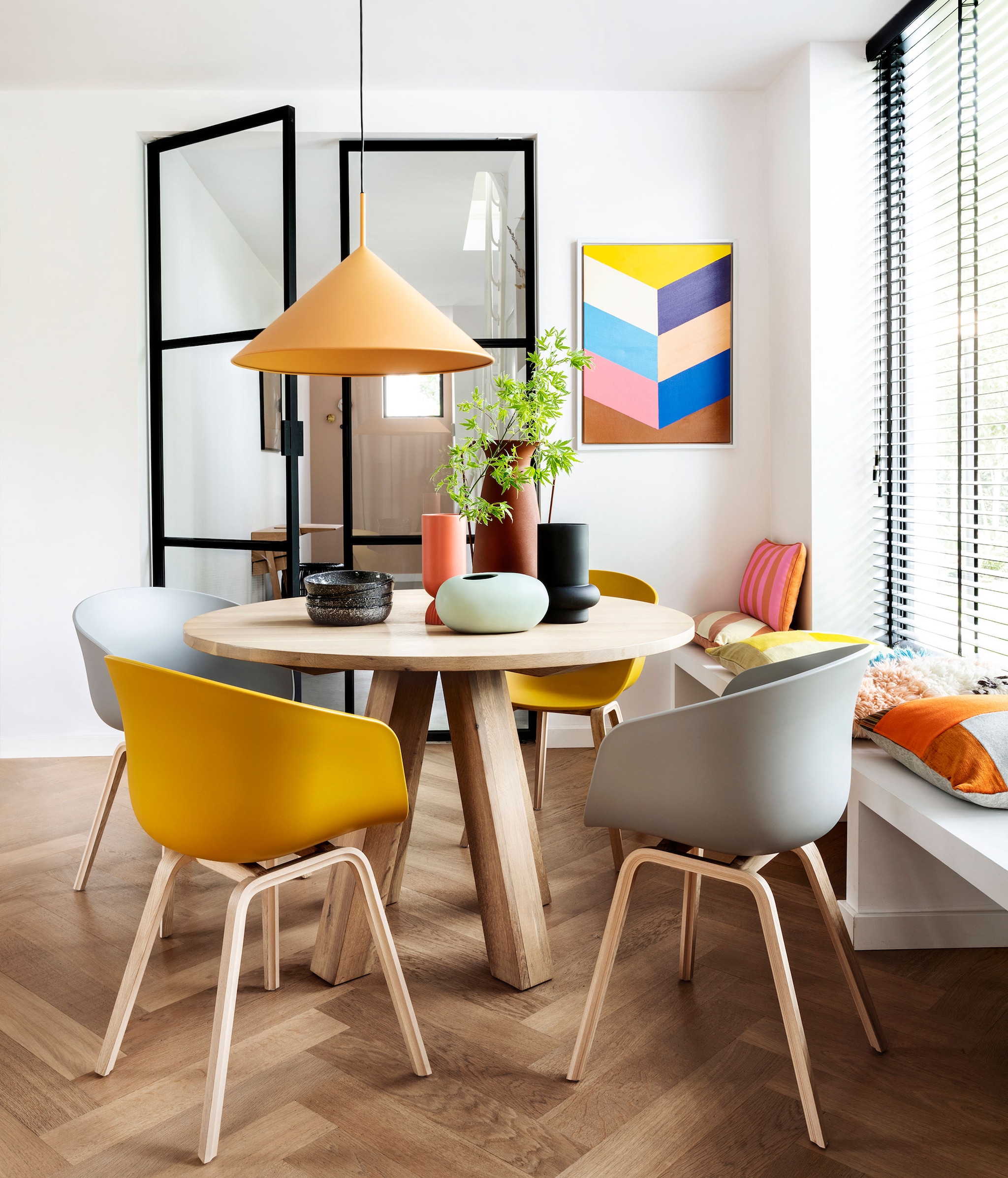 Eettafel Alaska, 120×78 cm (Øxh) € 1095,- (hetkabinet.nl). Eetkamerstoelen About a Chair van Hay in Mustard en Concrete,  Grey per stuk € 249,- (vtwonen.nl).,  Hanglamp Triangle, 60×39 cm (Øxh) € 239,-, schilderij Colourful Strokes € 139,95, oranje-roze gestreept kussen € 47,95, perzik crème gestreept kussen € 34,95, koraalrode vaas Suites Special € 27,95 (hkliving.nl). Wollen kussen Multi € 39,95, zwarte vaas Corsica,  € 17,50, borden Odile per stuk € 10,-, ovale mintkleurige vaas € 16,95 (loods5.nl). Kussen met oranje vlakken € 115,- (kus-sen.nl). Overig privébezit.