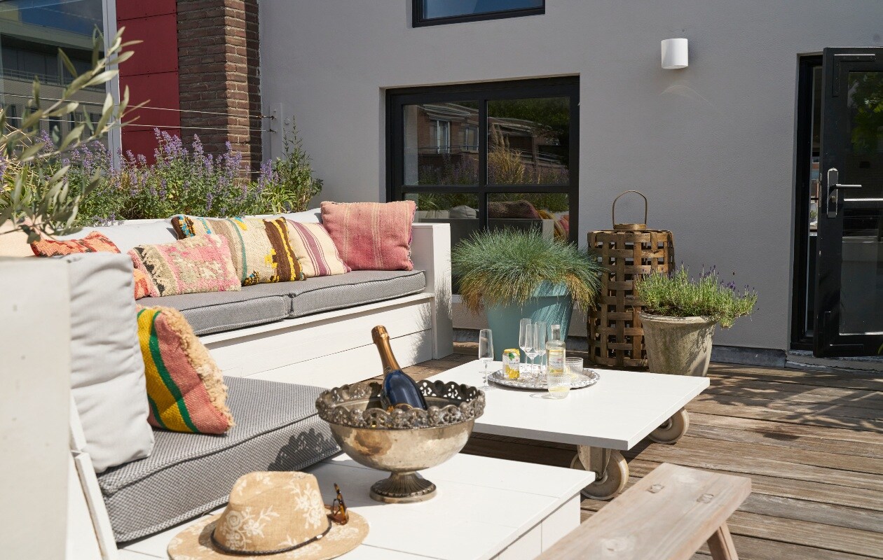 Loungemeubel en tafel op wielen eigen ontwerp. Kruk en geweven lantaarn Loods 5. Kussens op de bank Tim’s Kussens, kleurige kussens Bohemian du Maroc. Zilveren schaal op voet ooit bij de Bijenkorf gekocht