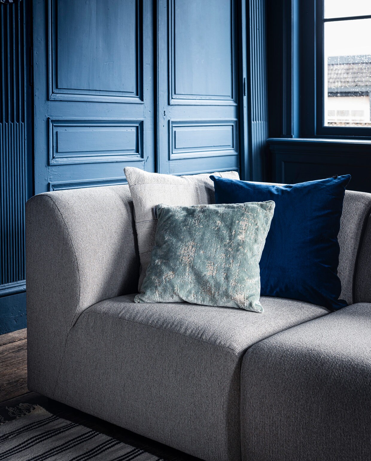 Bank Jax hkliving.nl, element vanaf € 499,- (vtwonen.nl). Kleed € 199,- (zarahome.com). Wit kussen Mrs.me € 99,- (homestede.nl). Blauw kussen € 49,-(couleurlocale.eu). Kussen Sarona vintage blue 45×45 cm € 35,- (polspotten.nl).