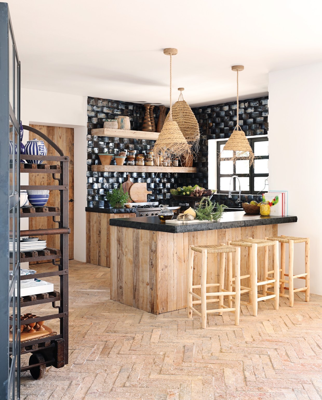 De keuken kreeg diepdonkerblauwe keramische tegels met een zweem zwart erin. De luxe glans steekt mooi af bij de natuurlijke materialen. Hanglampen Hubert Zandberg Interiors, barkrukken Mona Market. De aanrechtbladen zijn van zwart leisteen.